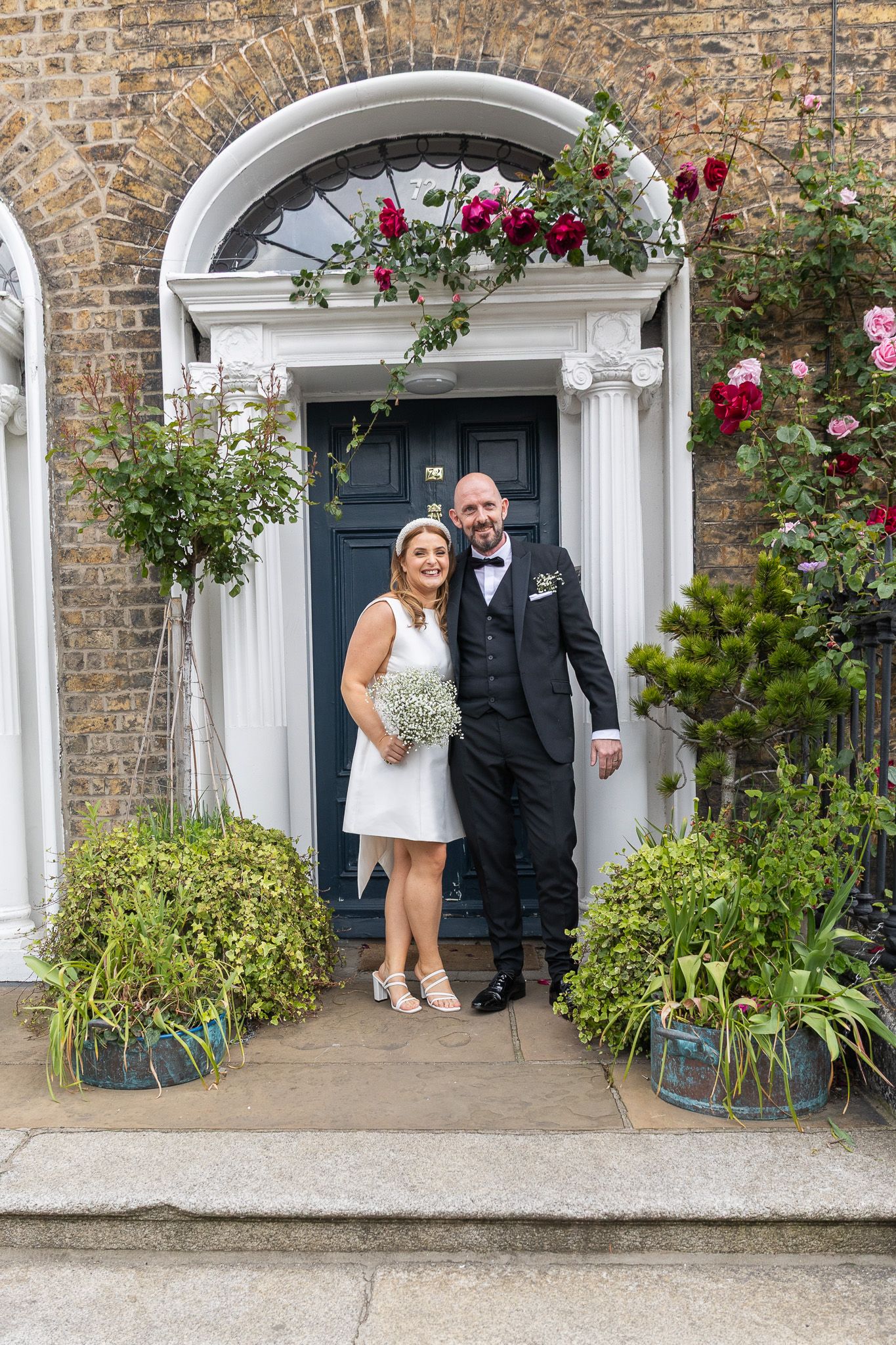 Couple poses in front of historic brick building with white columns and garden.