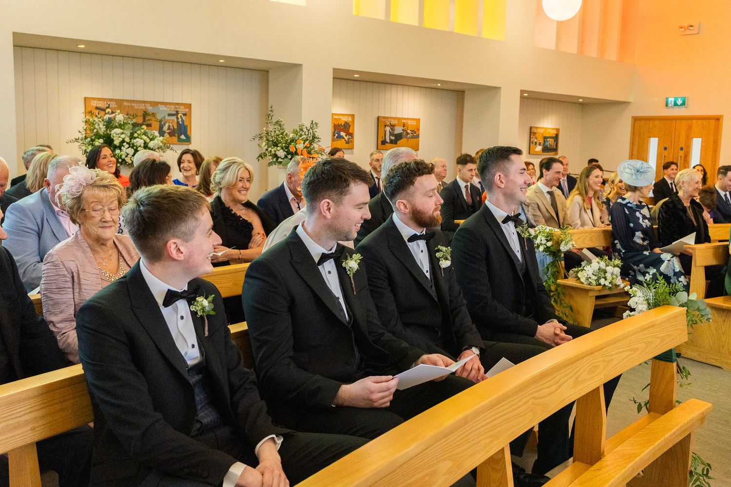 Wedding guests seated on wooden benches in a Dublin wedding chapel.