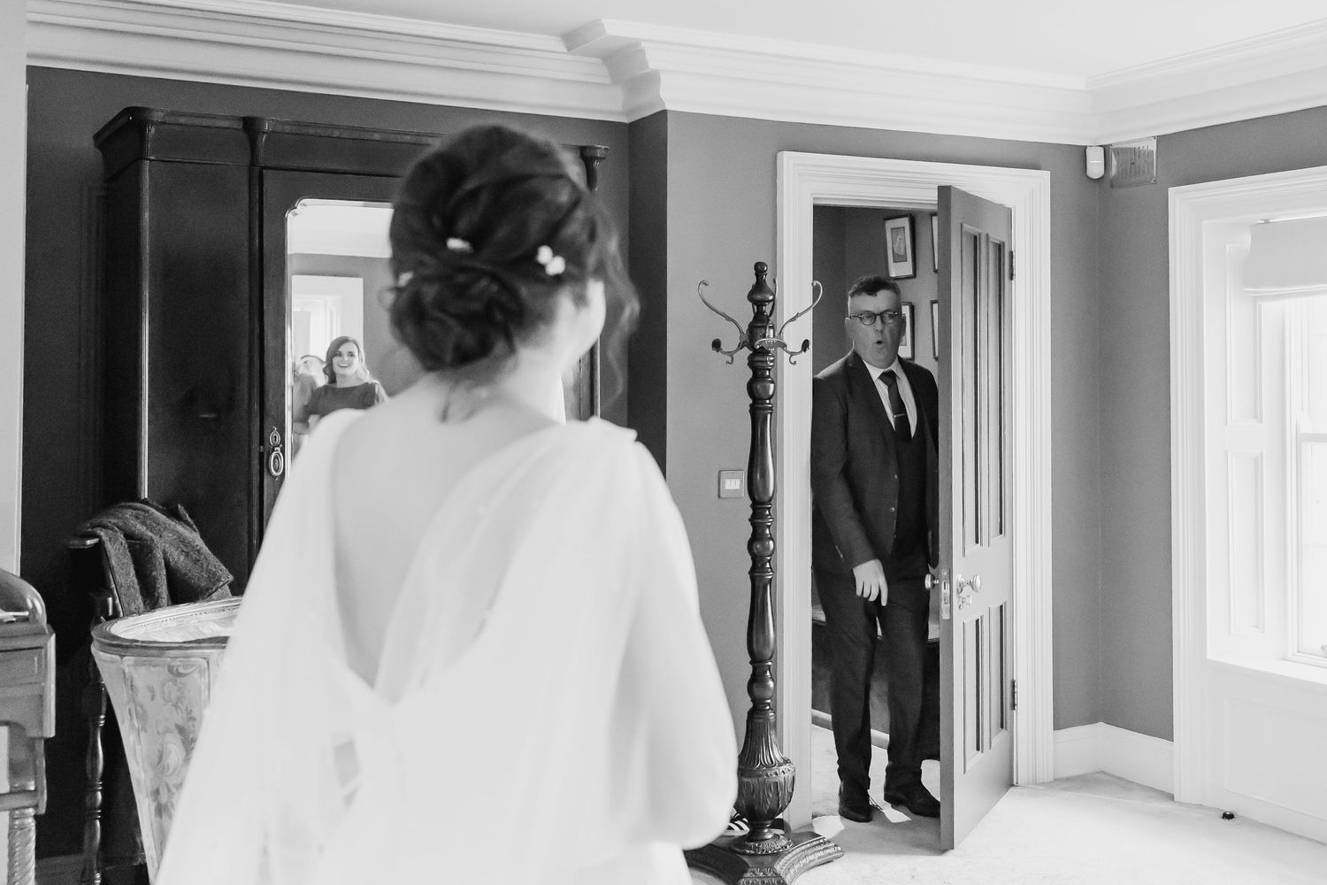 Black and white wedding photo of bride in elegant gown facing father having emotional first look moment.
