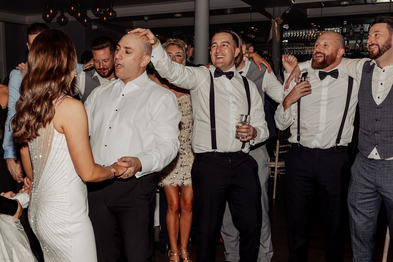 Wedding guests dancing and celebrating on a crowded dance floor at an evening reception.
