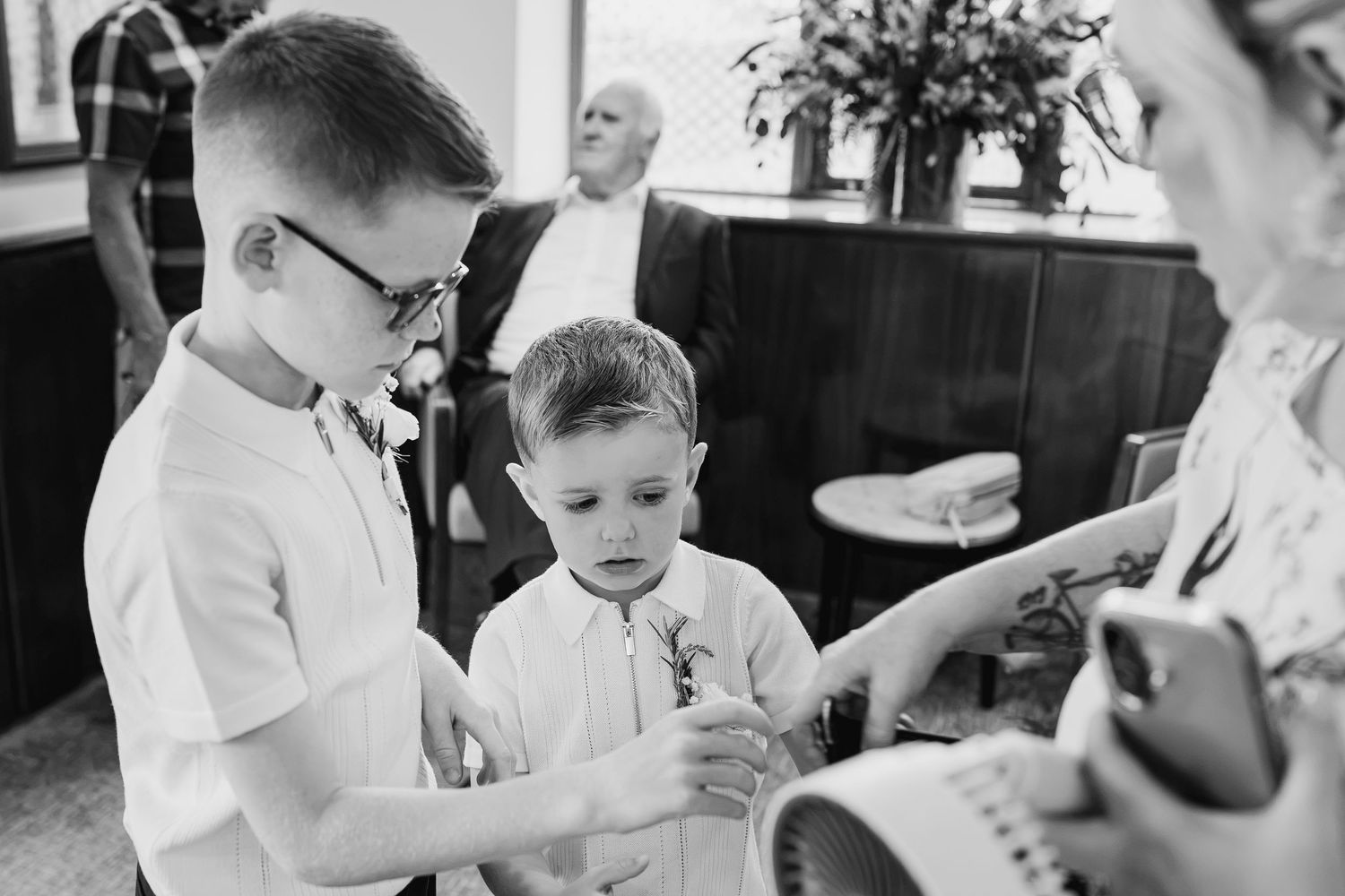 Two young boys in formal attire examine flowers at a wedding ceremony in black and white photo.