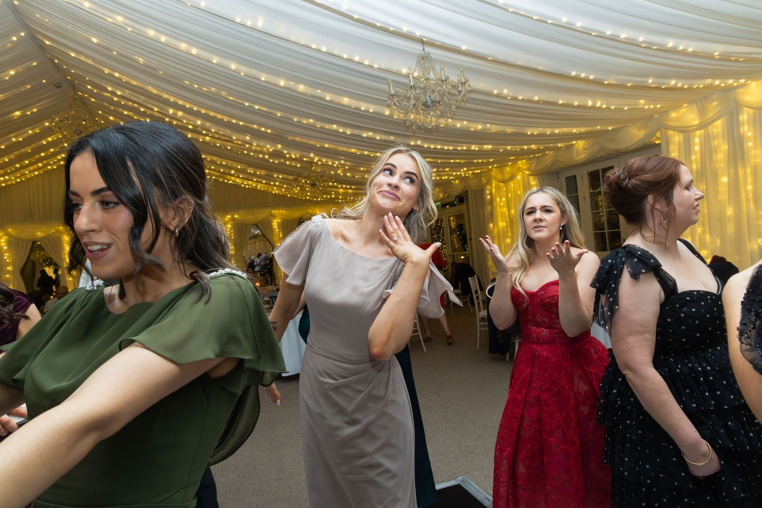 Women dancing and laughing at elegant wedding reception under sparkling fairy light canopy.
