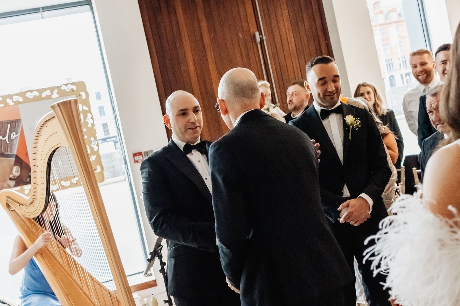 Wedding guests mingling in a bright indoor reception space with wooden doors.