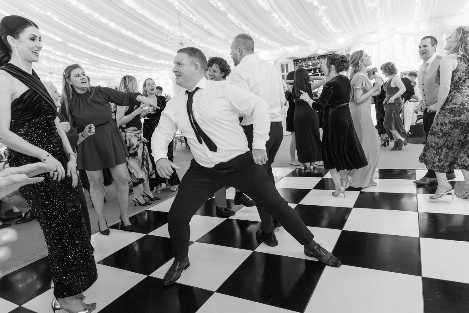 Energetic wedding guest performs dramatic dance move on checkered floor at lively wedding reception.