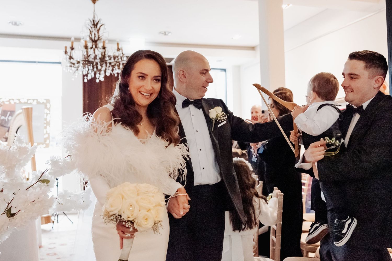 Elegant wedding reception celebration with guests enjoying a festive atmosphere under a crystal chandelier.