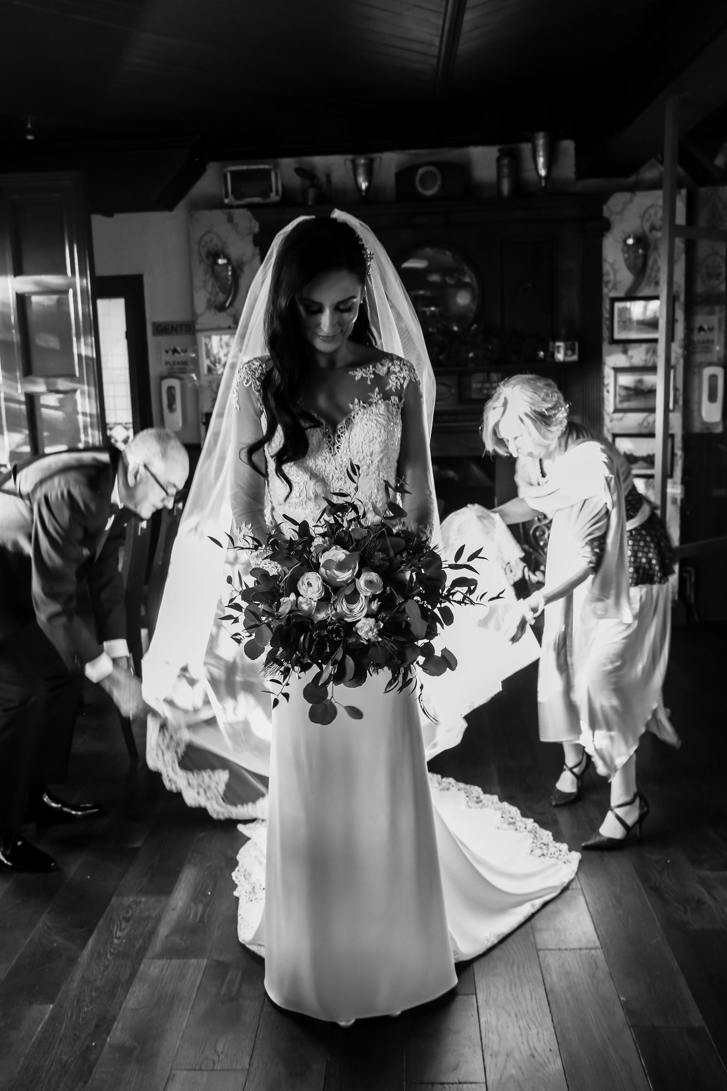 A bride in a white gown holds a colorful bouquet in a dimly lit room.