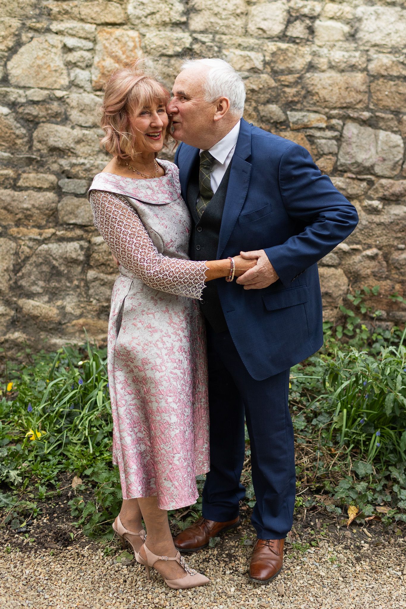 An elderly couple shares a romantic moment against a stone wall backdrop in a garden setting Dublin.