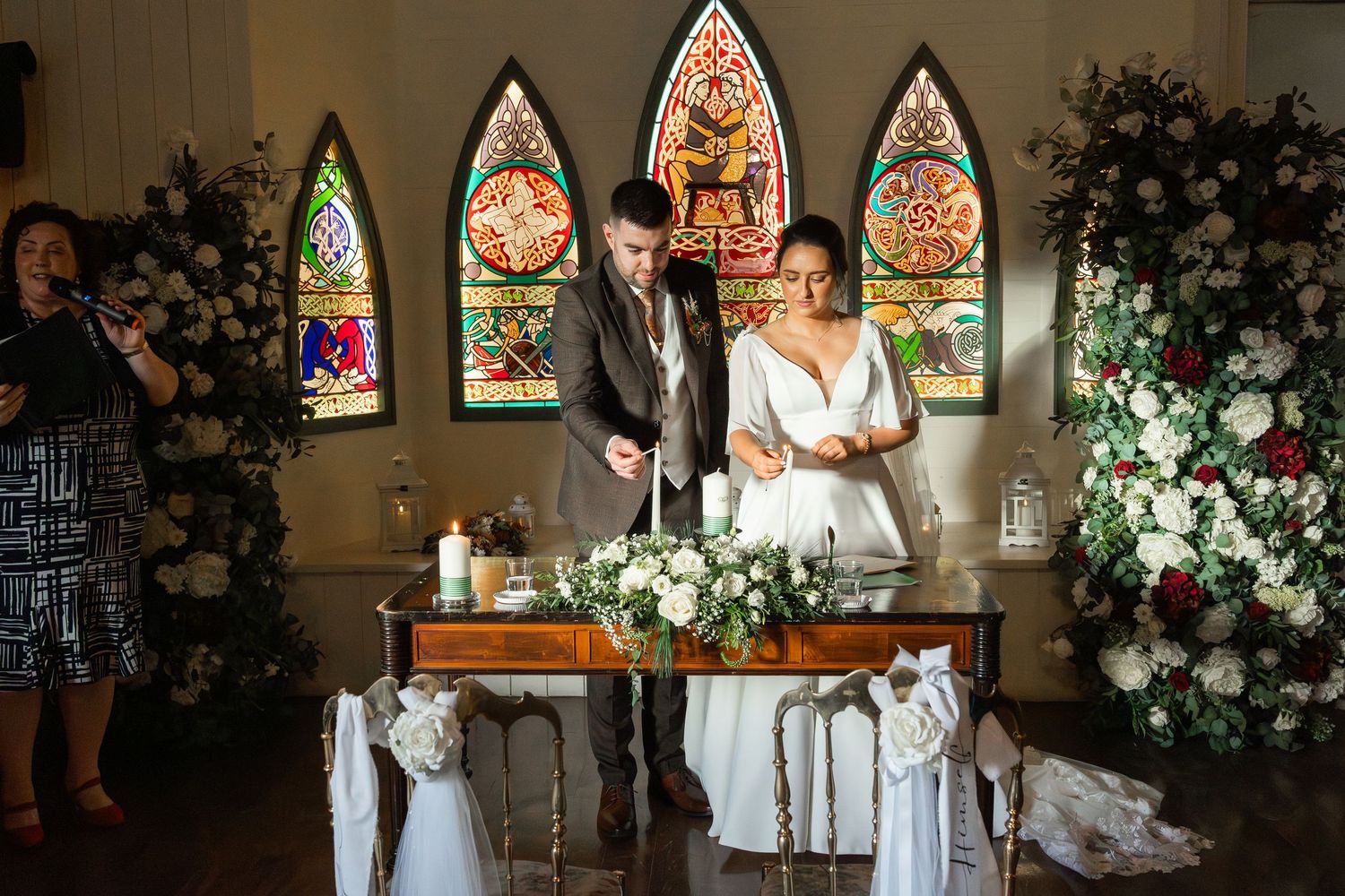 Bride and groom signing wedding register at ceremony altar with stained glass windows.