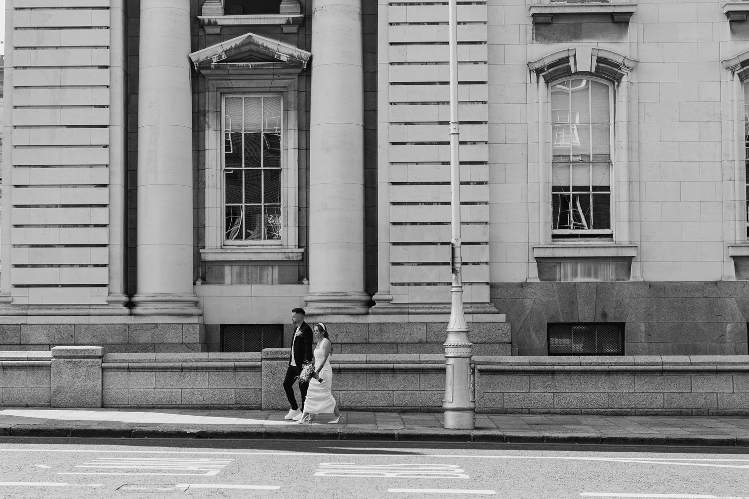 A couple walks past a grand neoclassical building in this black and white street photo.