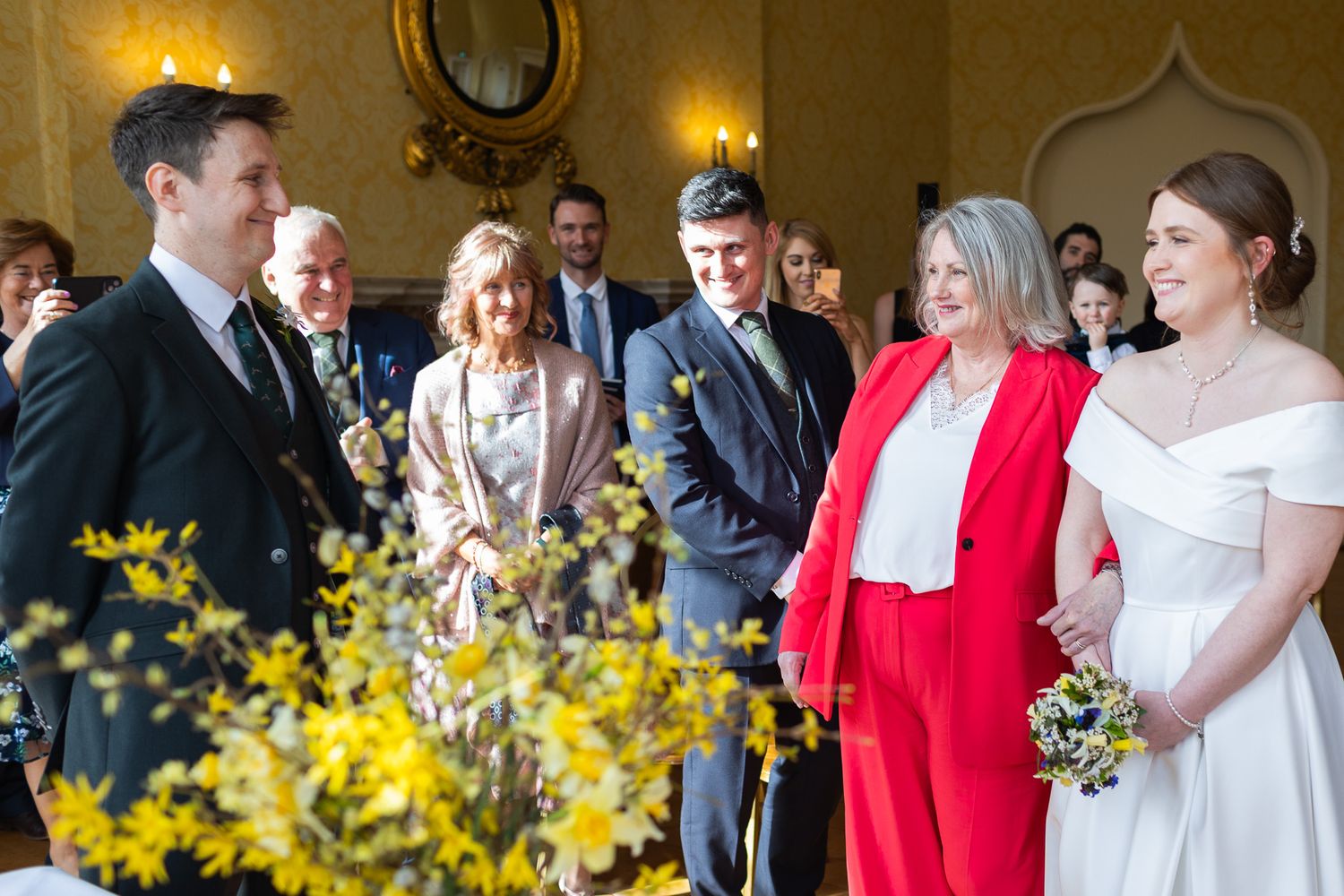 Wedding guests gather in an elegant room with gold walls and decorative sconces for a celebration in Dublin City.