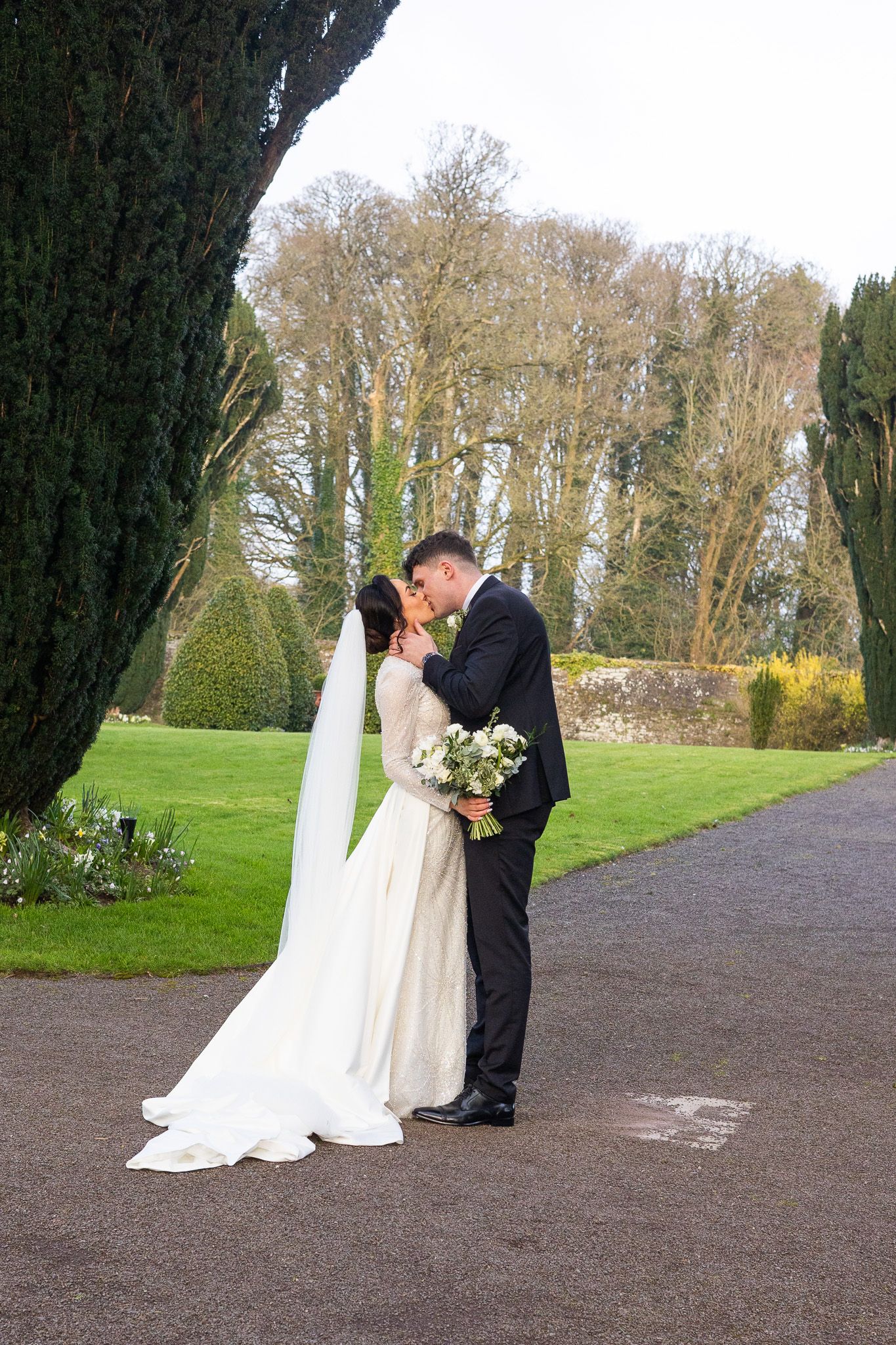 Couple in wedding attire captured by Dublin city wedding photographer walking along a scenic garden pathway in Tankardstown.