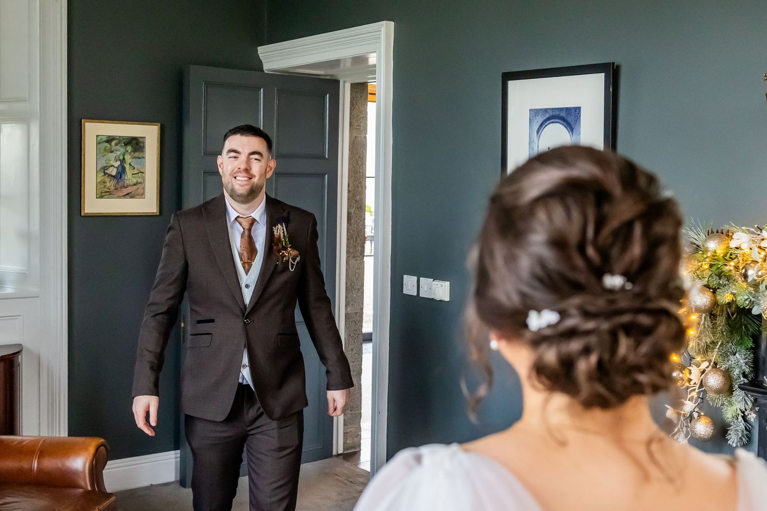 Groom in dark suit smiles at bride during first look moment in elegant room with teal walls.