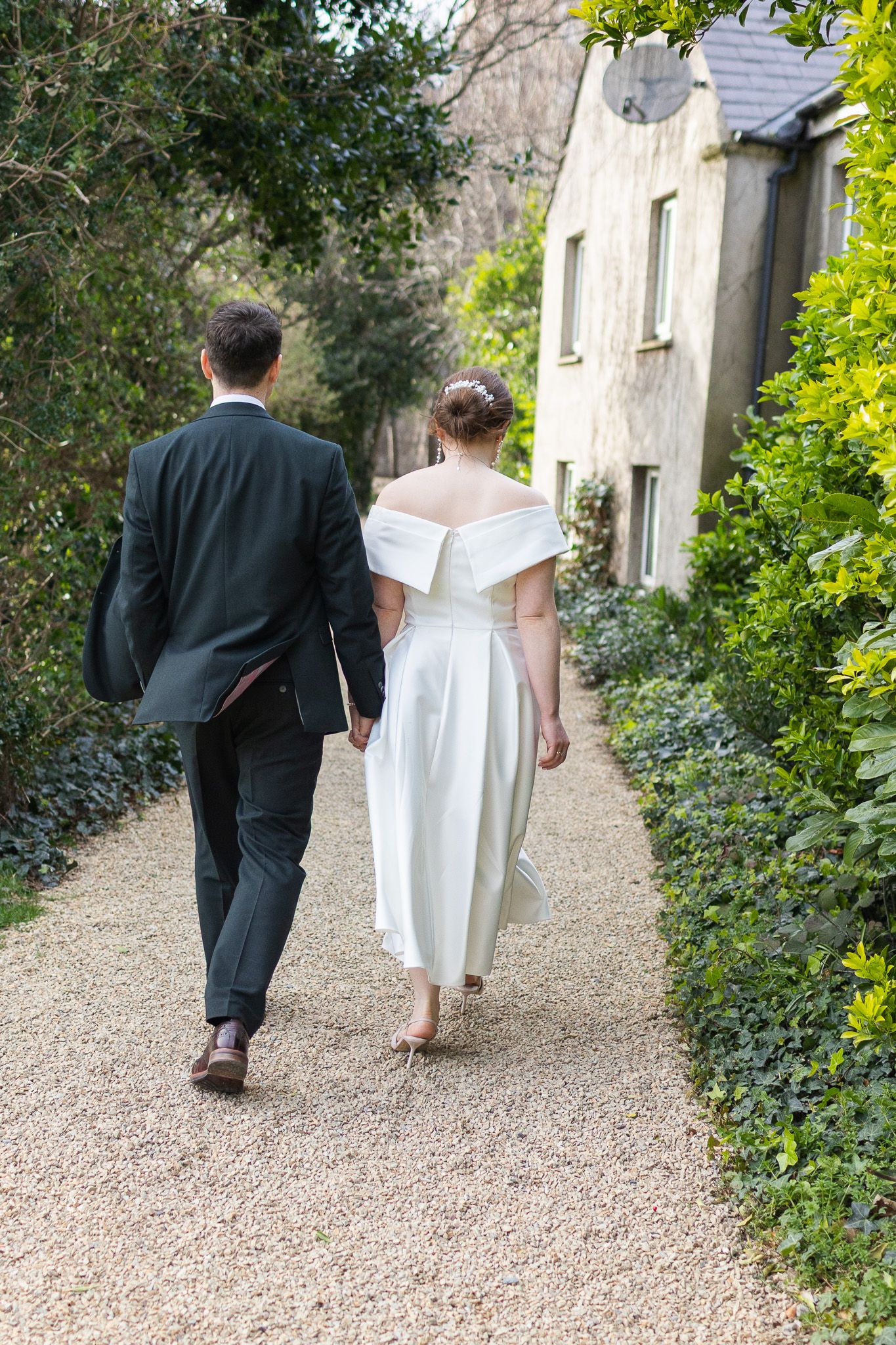 A couple walking down a gravel path lined with greenery outside a Dublin City stone building.