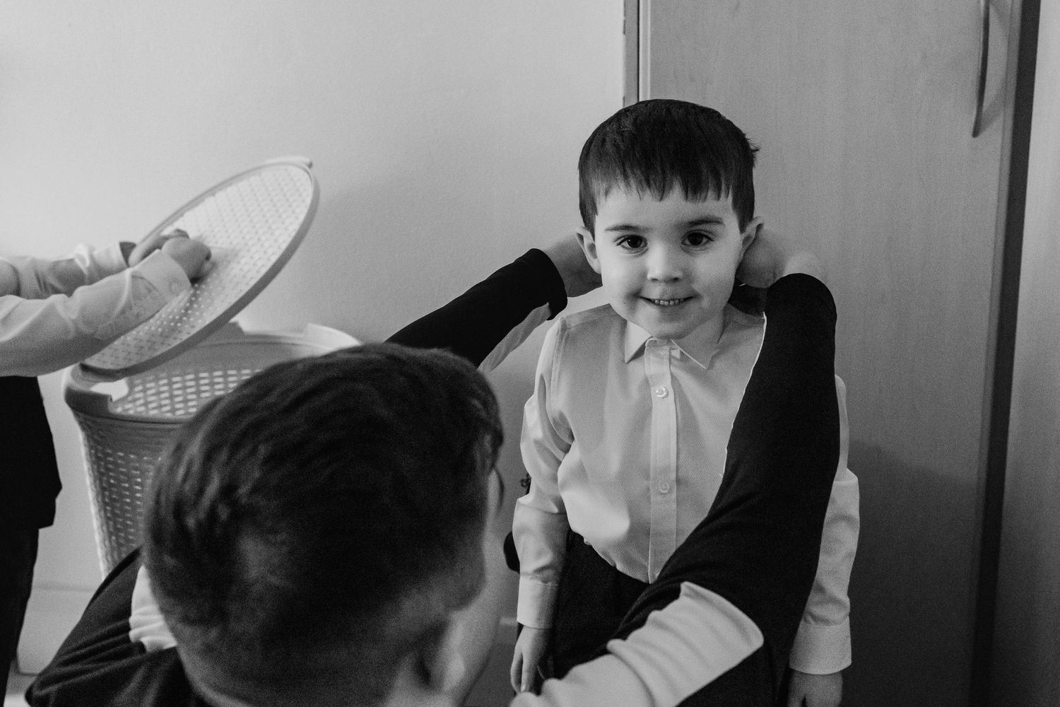 Black and white photo of a young boy in dress shirt smiling at someone during a formal event.