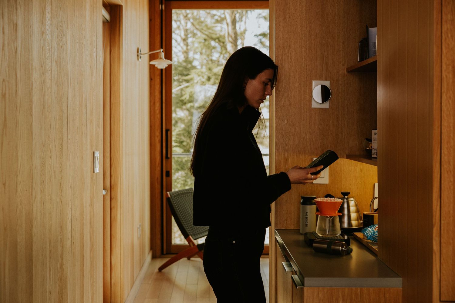 Woman in black outfit setting up coffee station in modern wood-paneled kitchen with natural light at Piaule Catskill. Shot by Dylan spangler