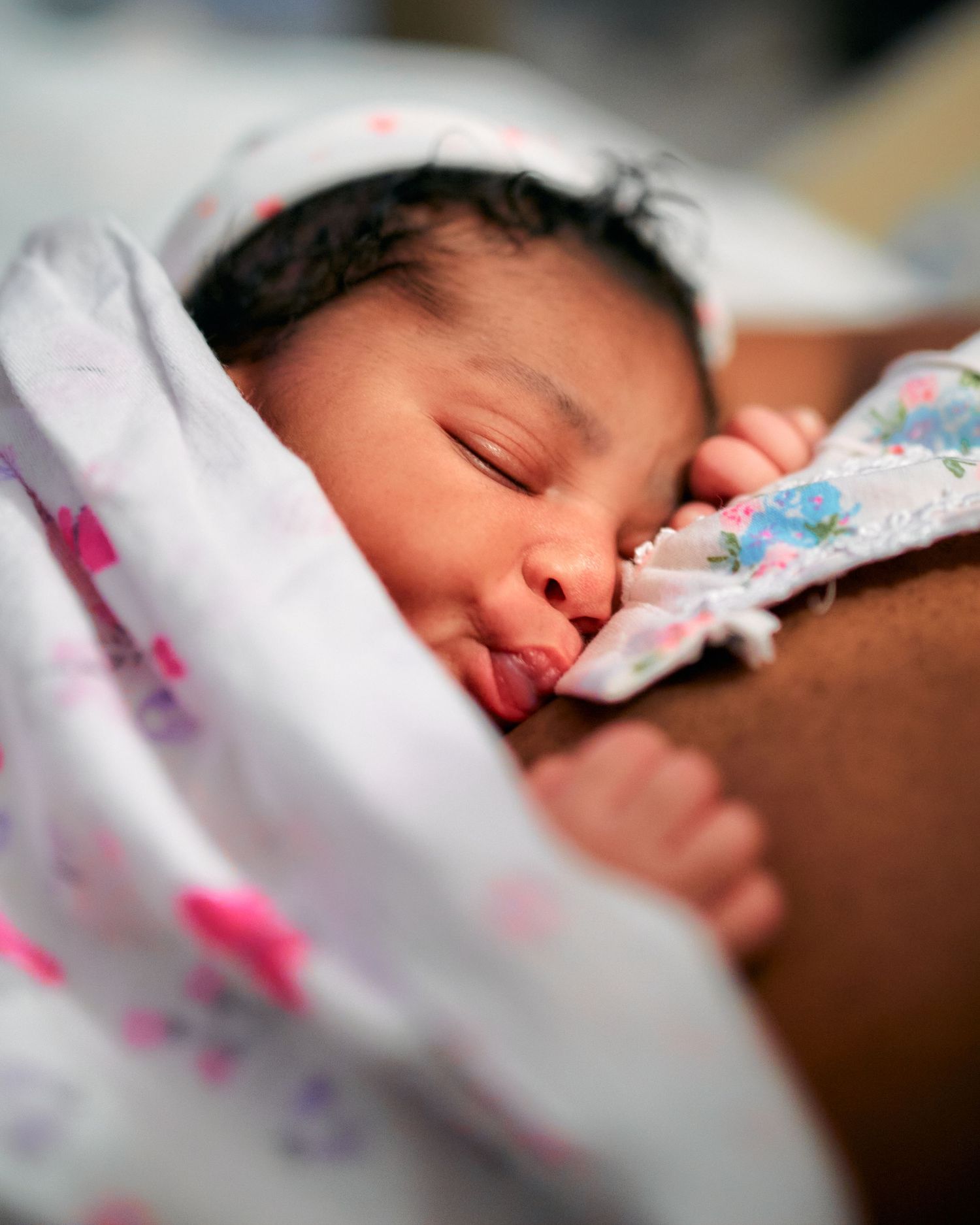Sleeping baby wrapped in a white floral patterned blanket rests peacefully in close-up view.