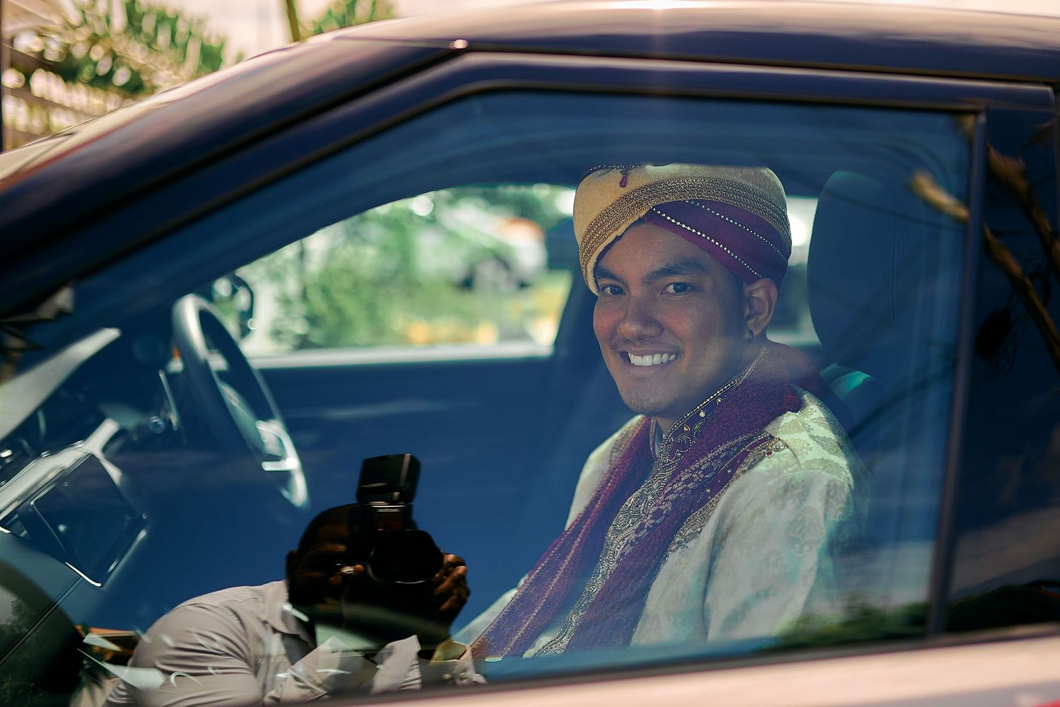 Groom in traditional Indian attire sitting in car with joyful expression.
