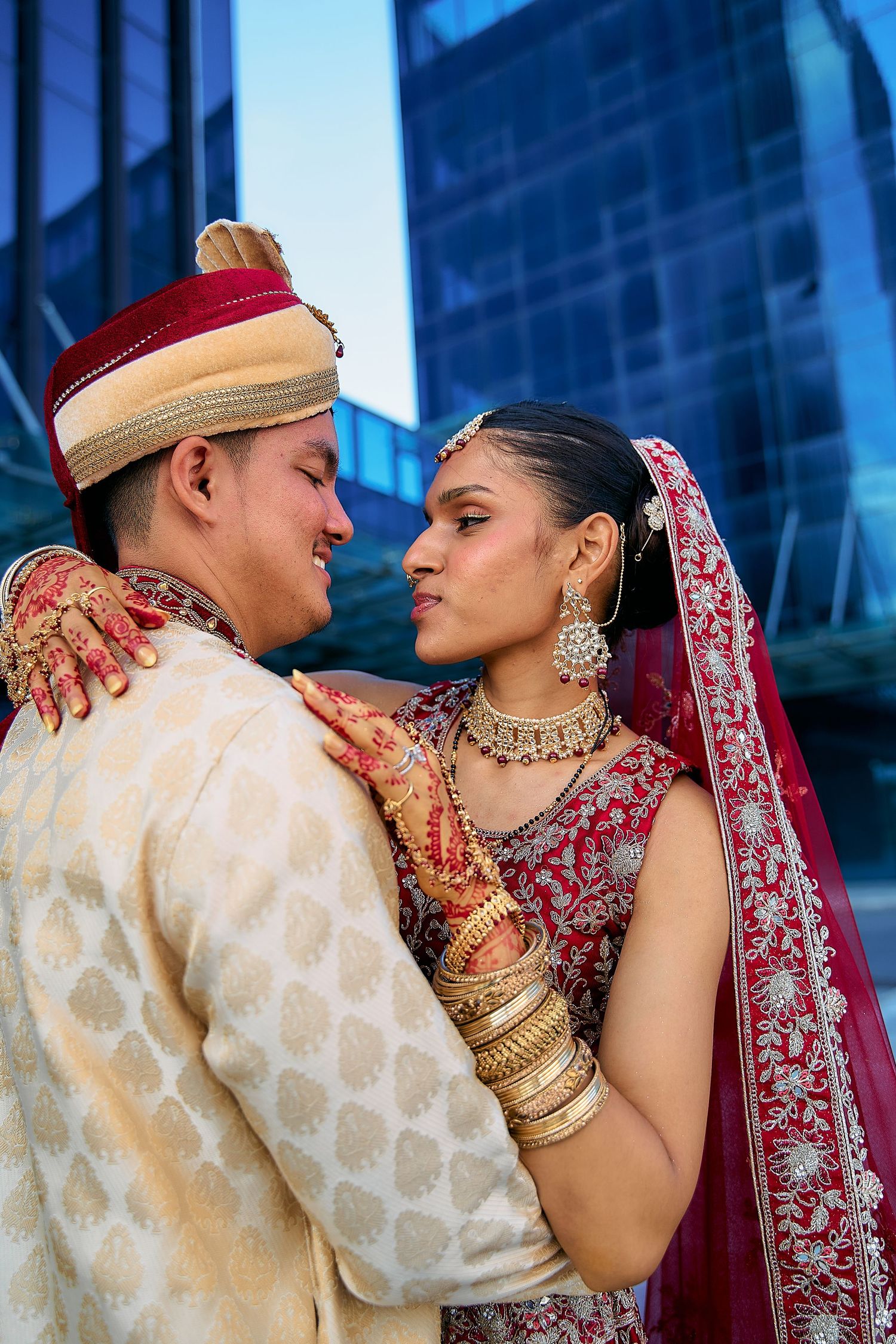 Romantic couple portraits against modern building backdrop in traditional Indian wedding outfits.