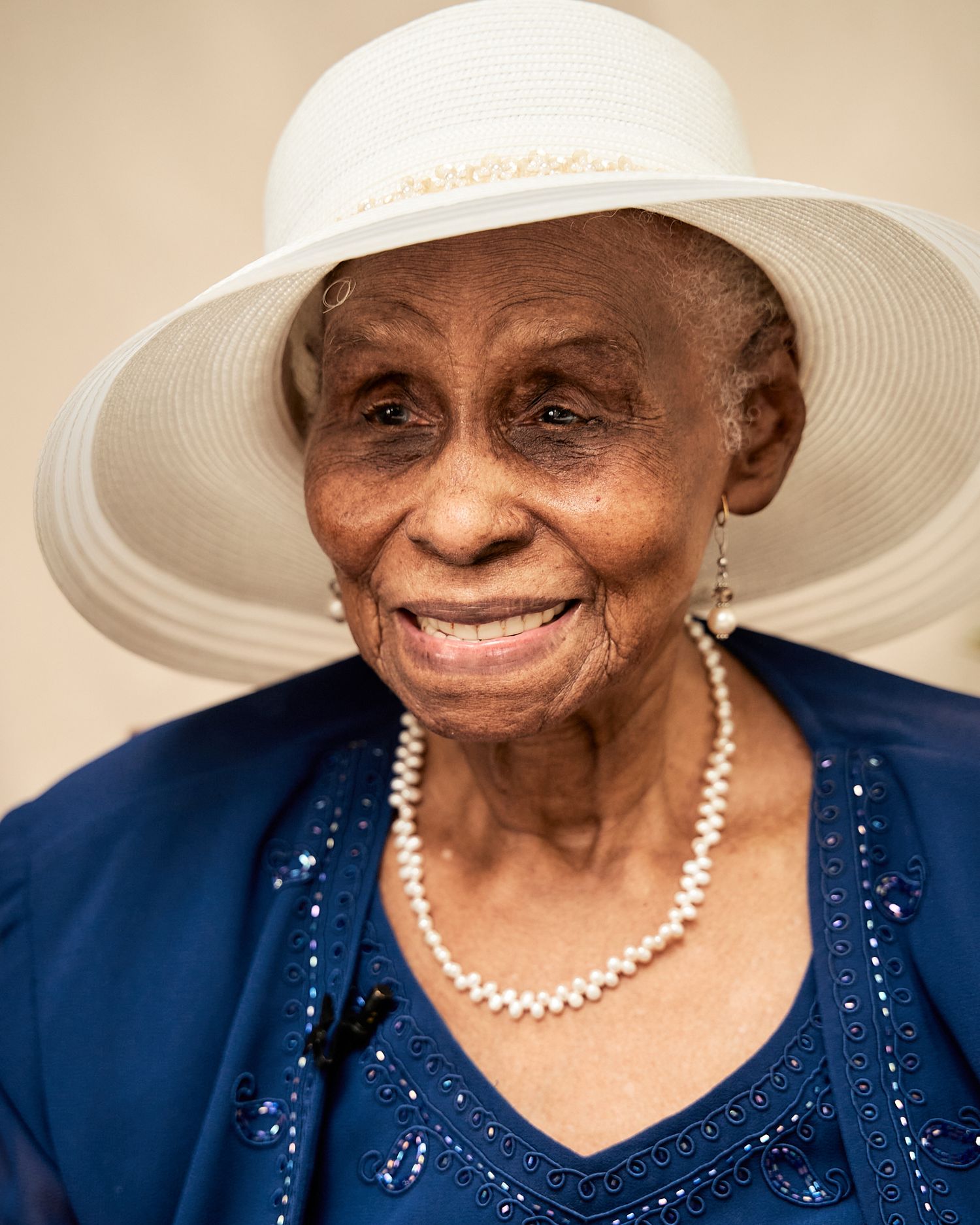 Elegant senior wearing a navy sequined dress and white sun hat in a portrait series.