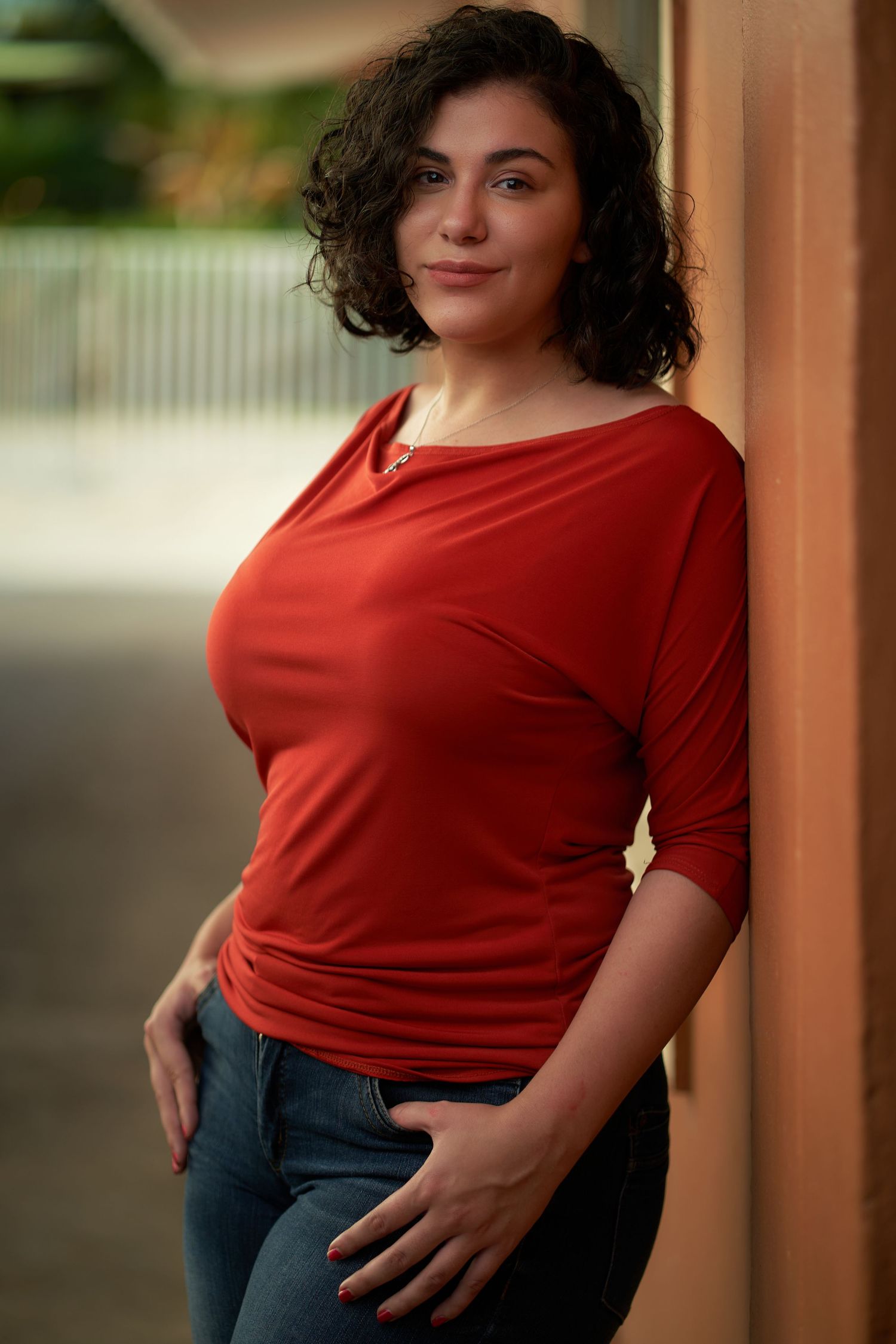 Person wearing a red t-shirt and jeans poses against a warm-toned background in a casual portrait series.