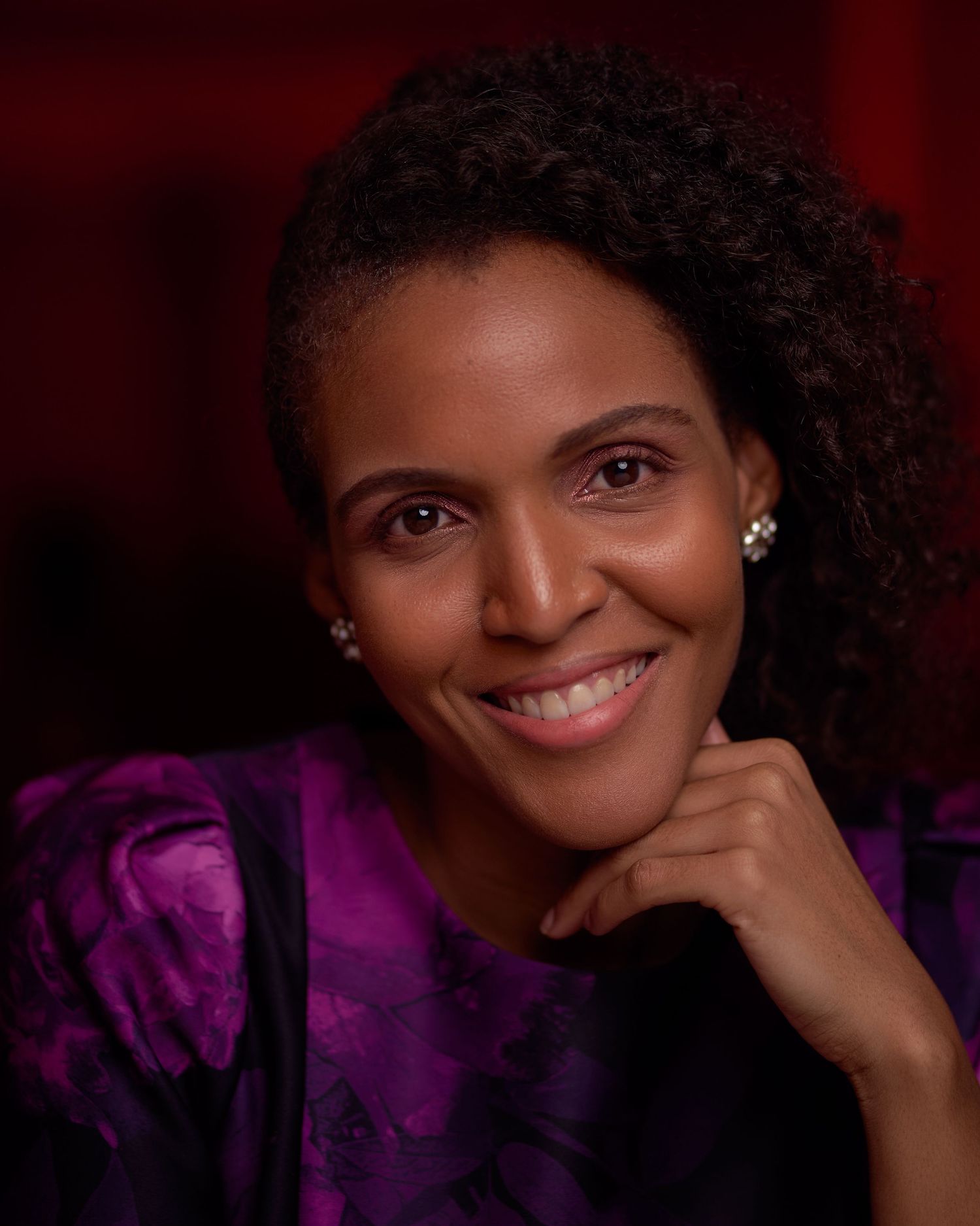 Professional studio portrait of a person in a purple blouse against a dark red background.