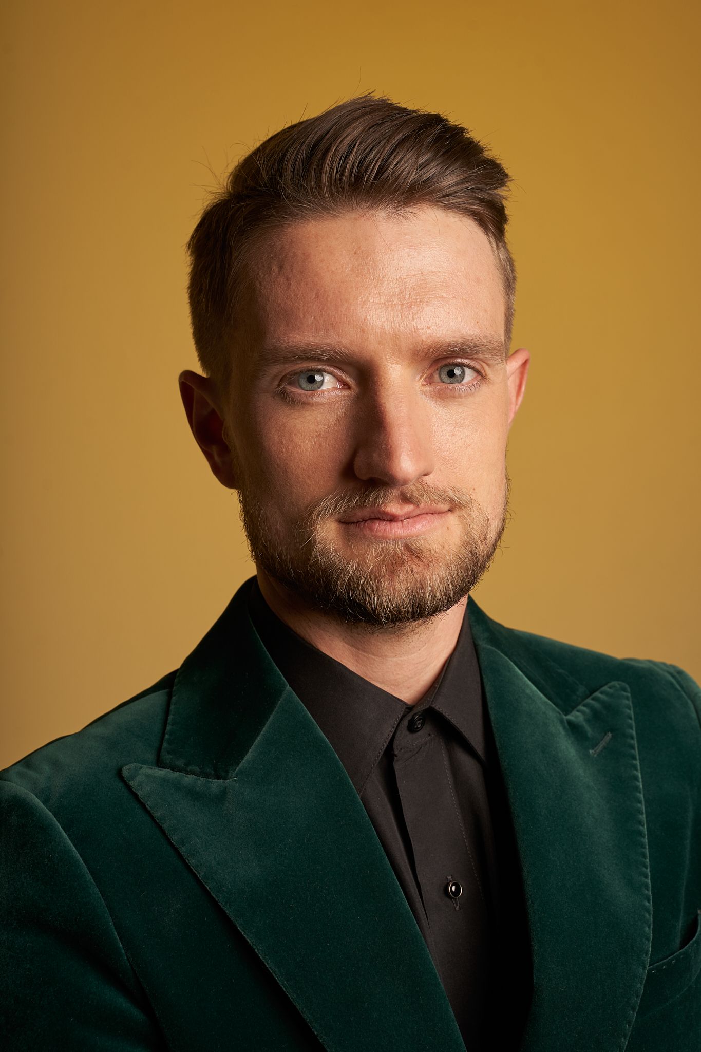 Professional portraits of someone in emerald velvet blazer against warm gold background.