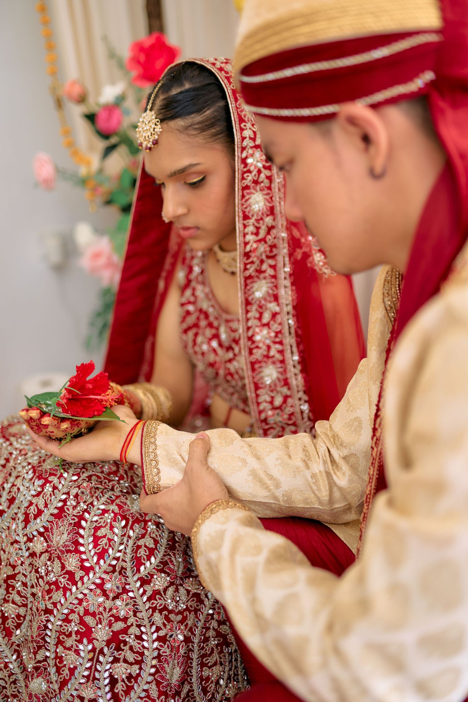 Traditional Indian wedding ceremony showing close-up details of bride and groom in ornate red and gold attire.