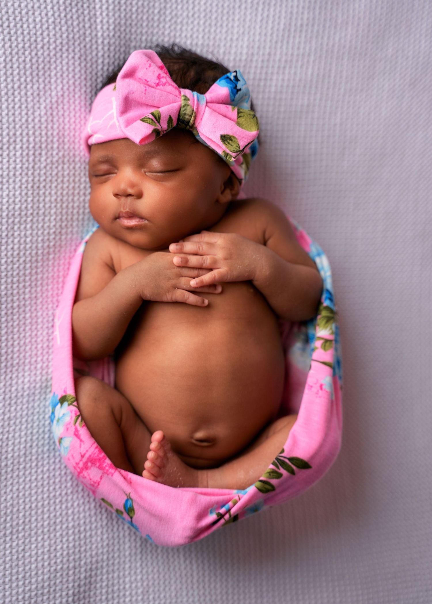 Sleeping newborn wearing pink headband and floral wrap captured in multiple artistic angles on grey backdrop.