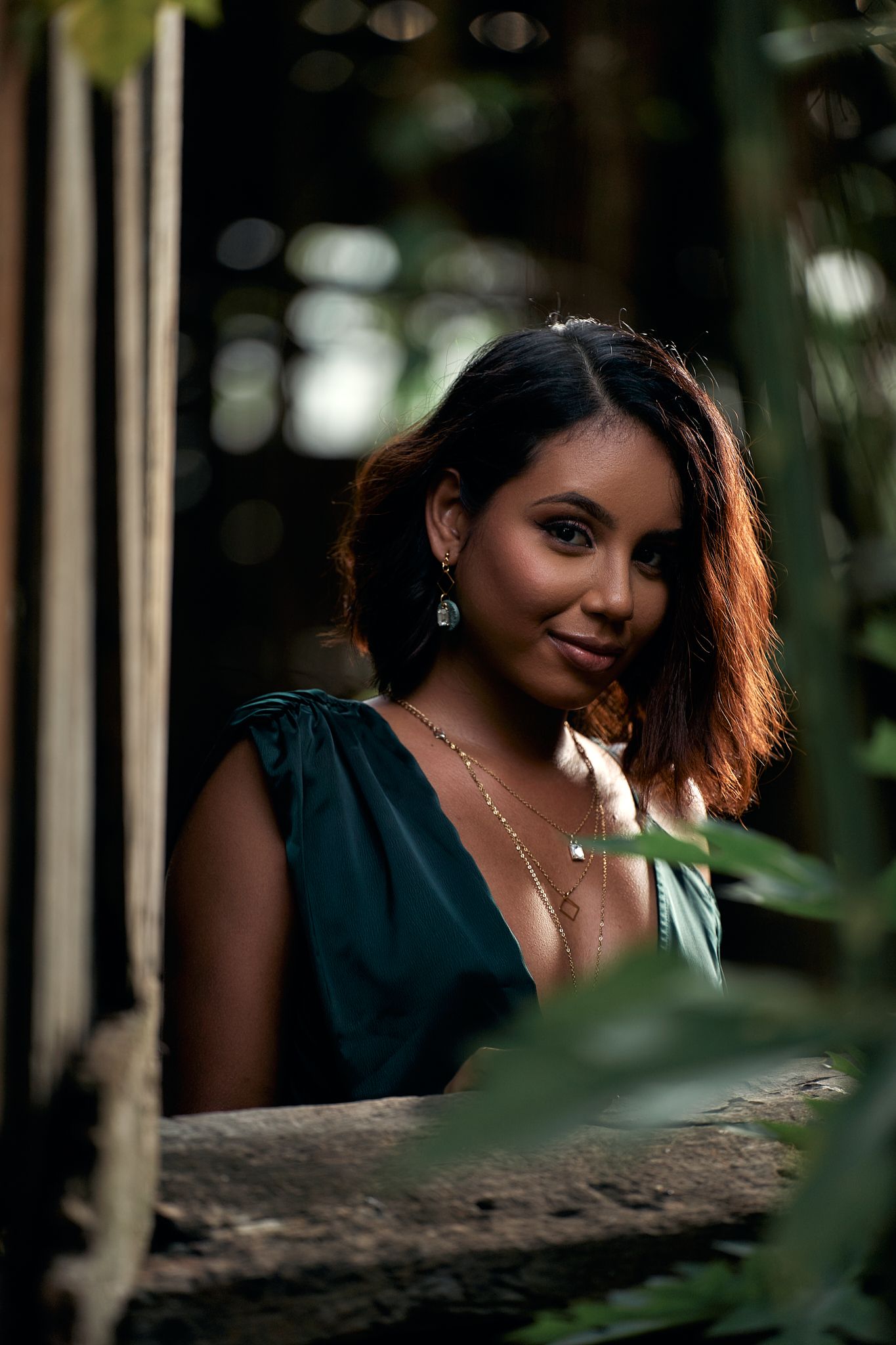 Artistic portrait through foliage with natural lighting and jewelry details.