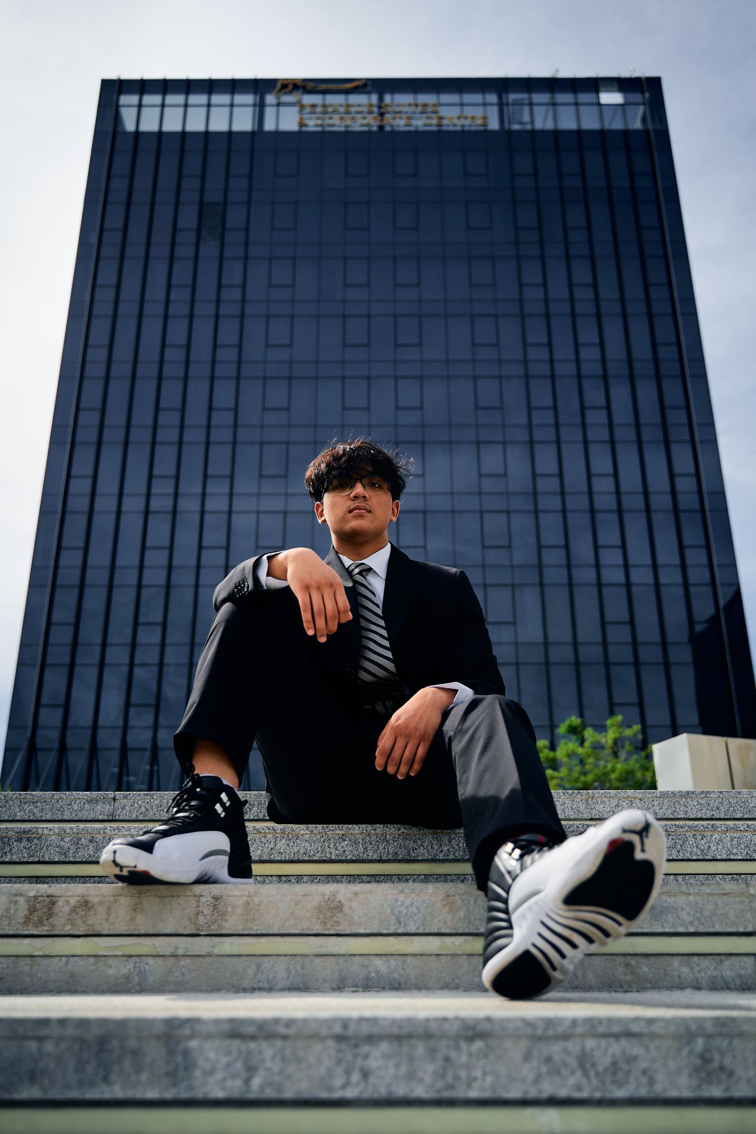 Low angle shot of a person in business attire sitting on steps with modern office building behind them.