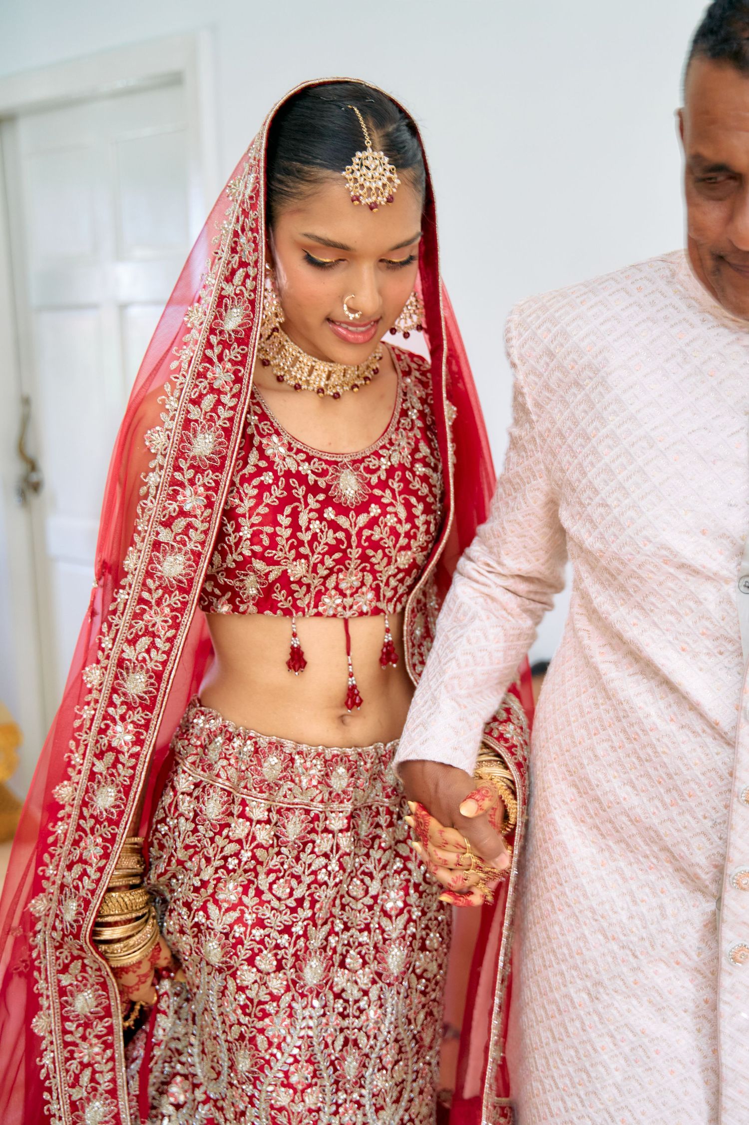 Couple in traditional red and cream Indian wedding outfits during ceremony rituals.