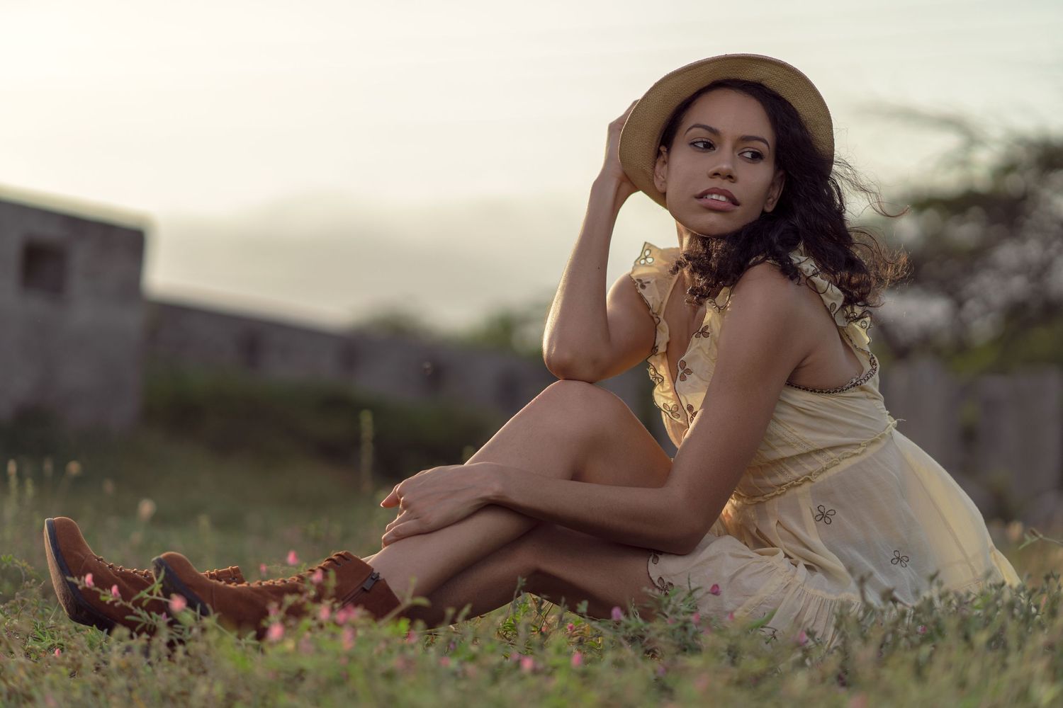Outdoor portrait of a person in a cream dress sitting on grass at sunset.