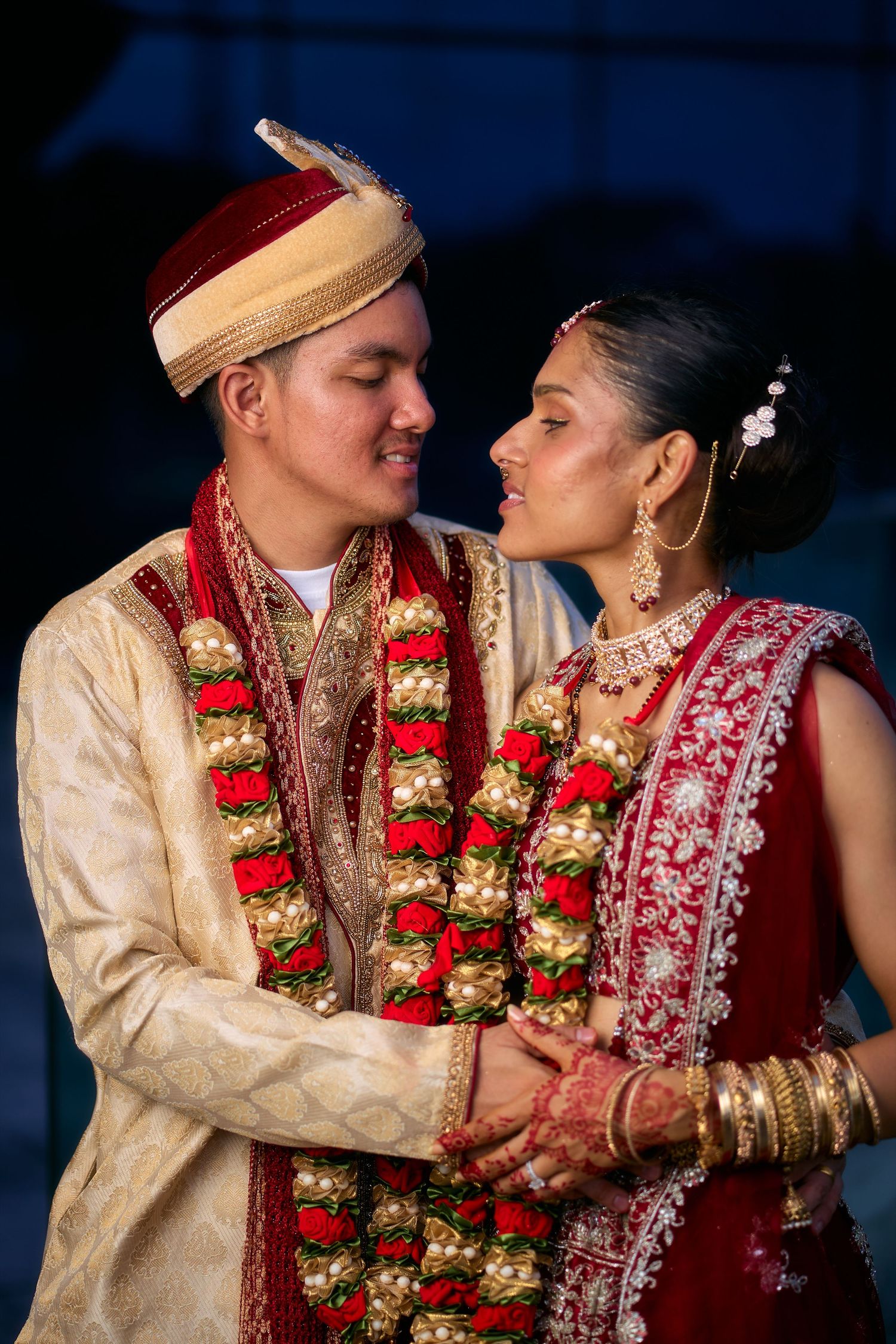 Couple in traditional Indian wedding attire share intimate moments wearing flower garlands.