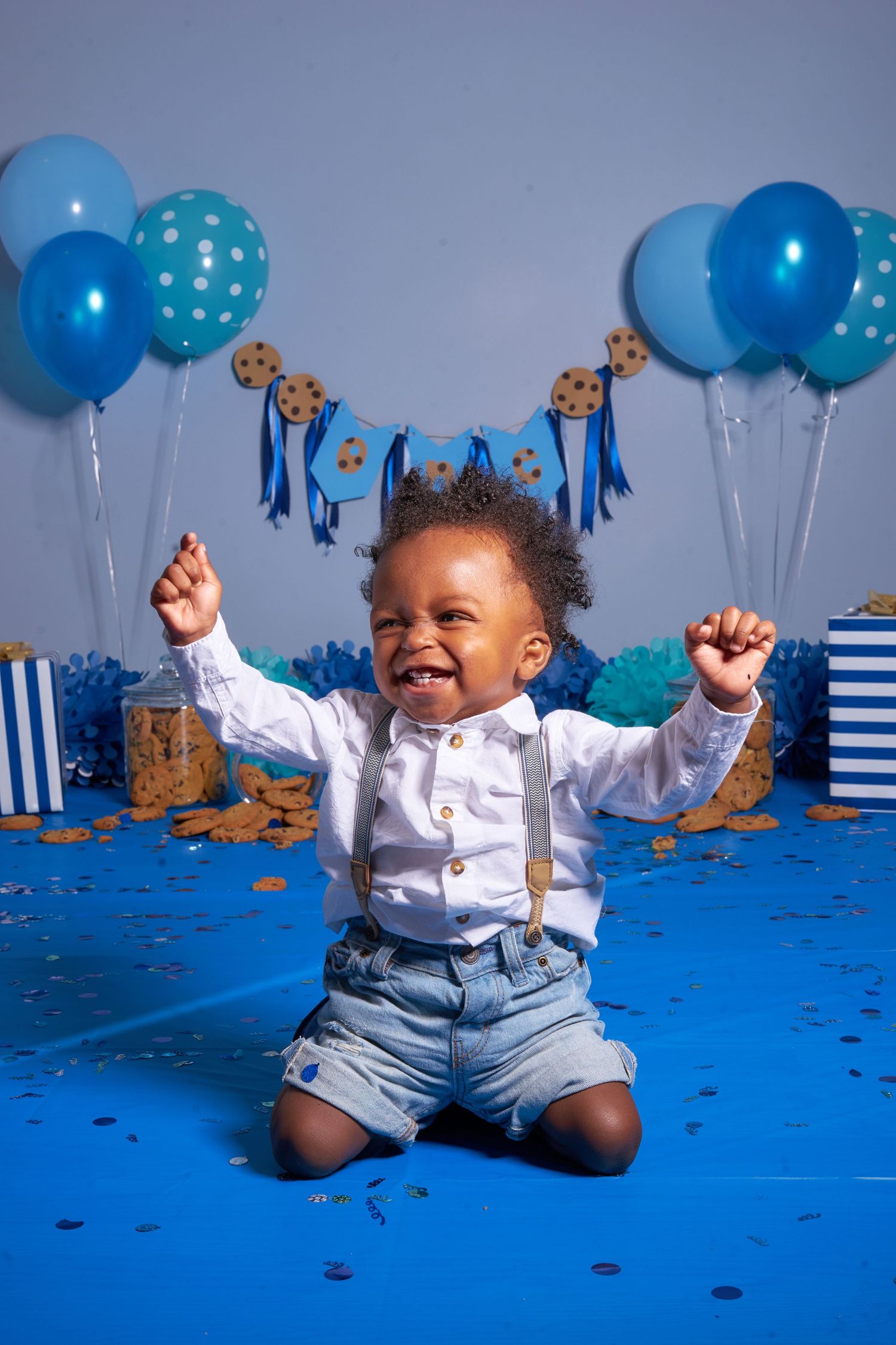 Festive first birthday party setup with blue balloons, decorations and confetti on bright blue backdrop.