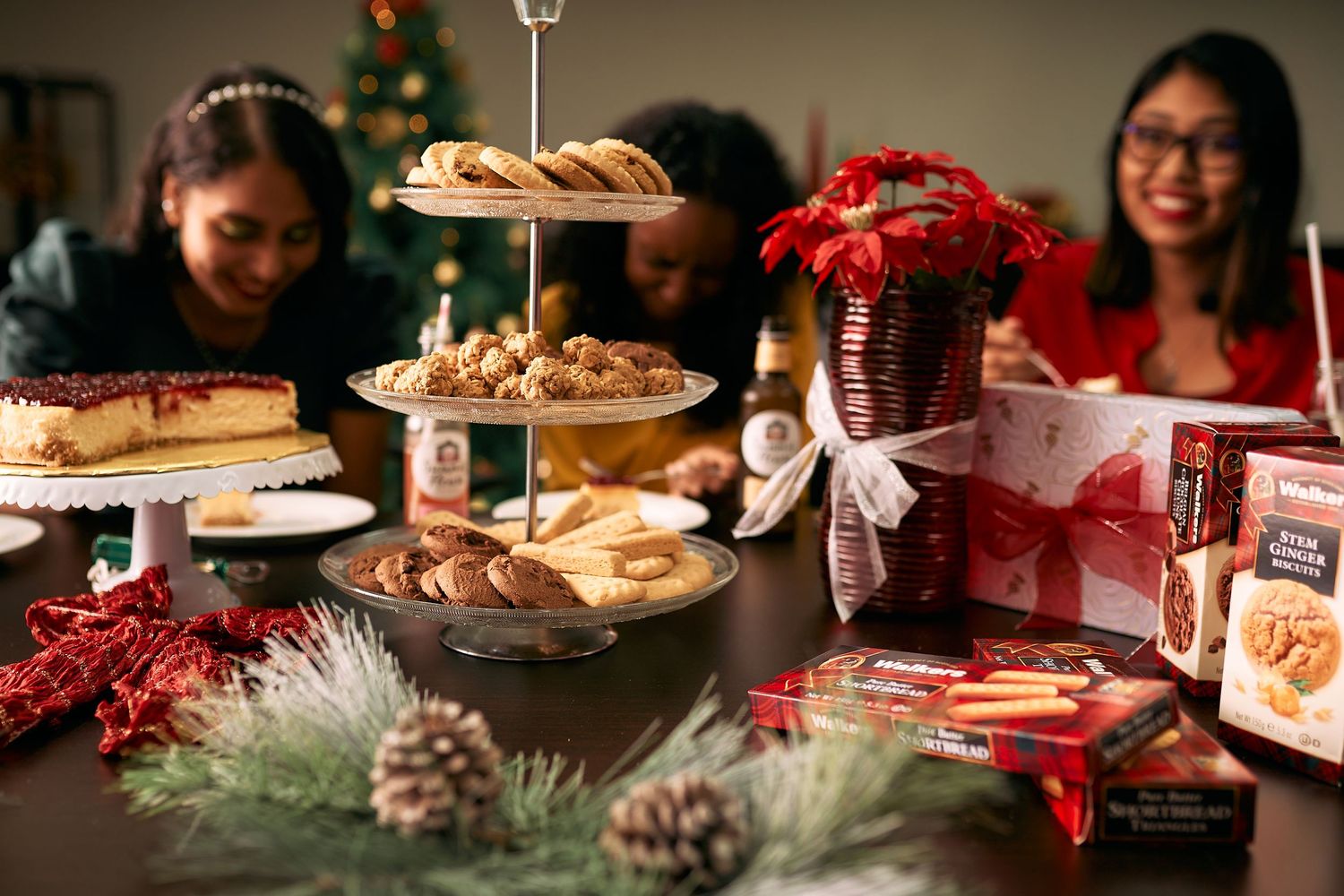 A festive holiday table with tiered dessert stand, Christmas decorations, and people gathered for a celebration.