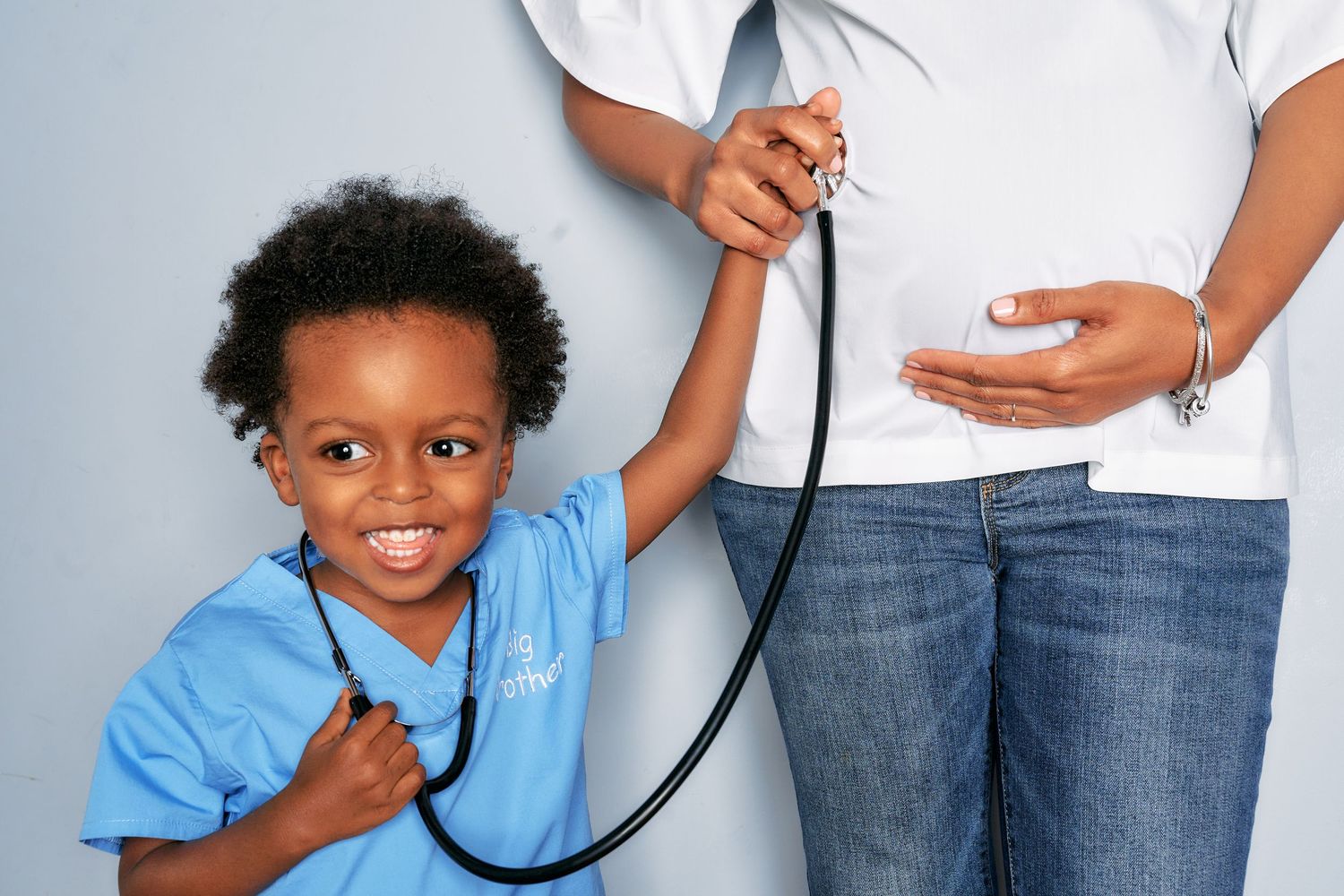 Child in blue shirt with stethoscope next to adult in white shirt and jeans.