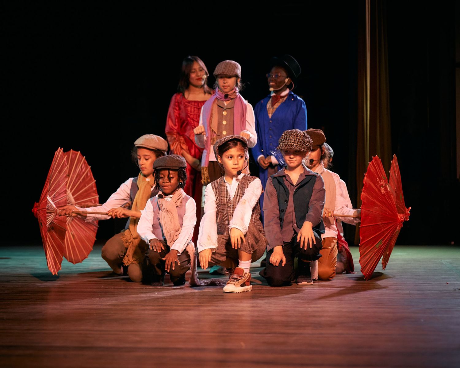 Performers in casual attire sit on stage with red props during a theatrical production.