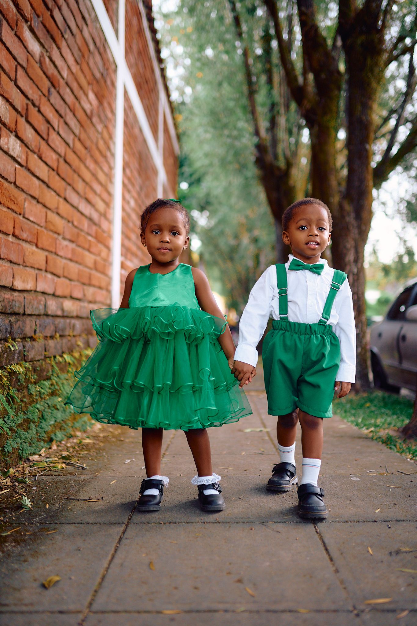 Children in green and white outfits sitting on a brick-lined path outdoors.