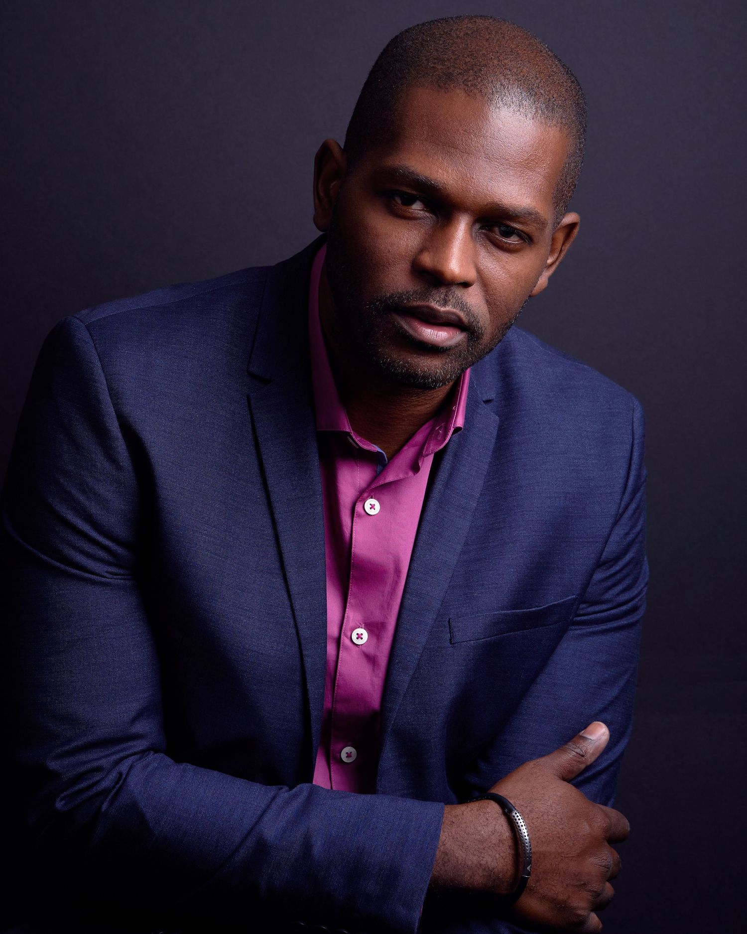 Professional portraits of someone in navy suit and pink shirt against dark background.