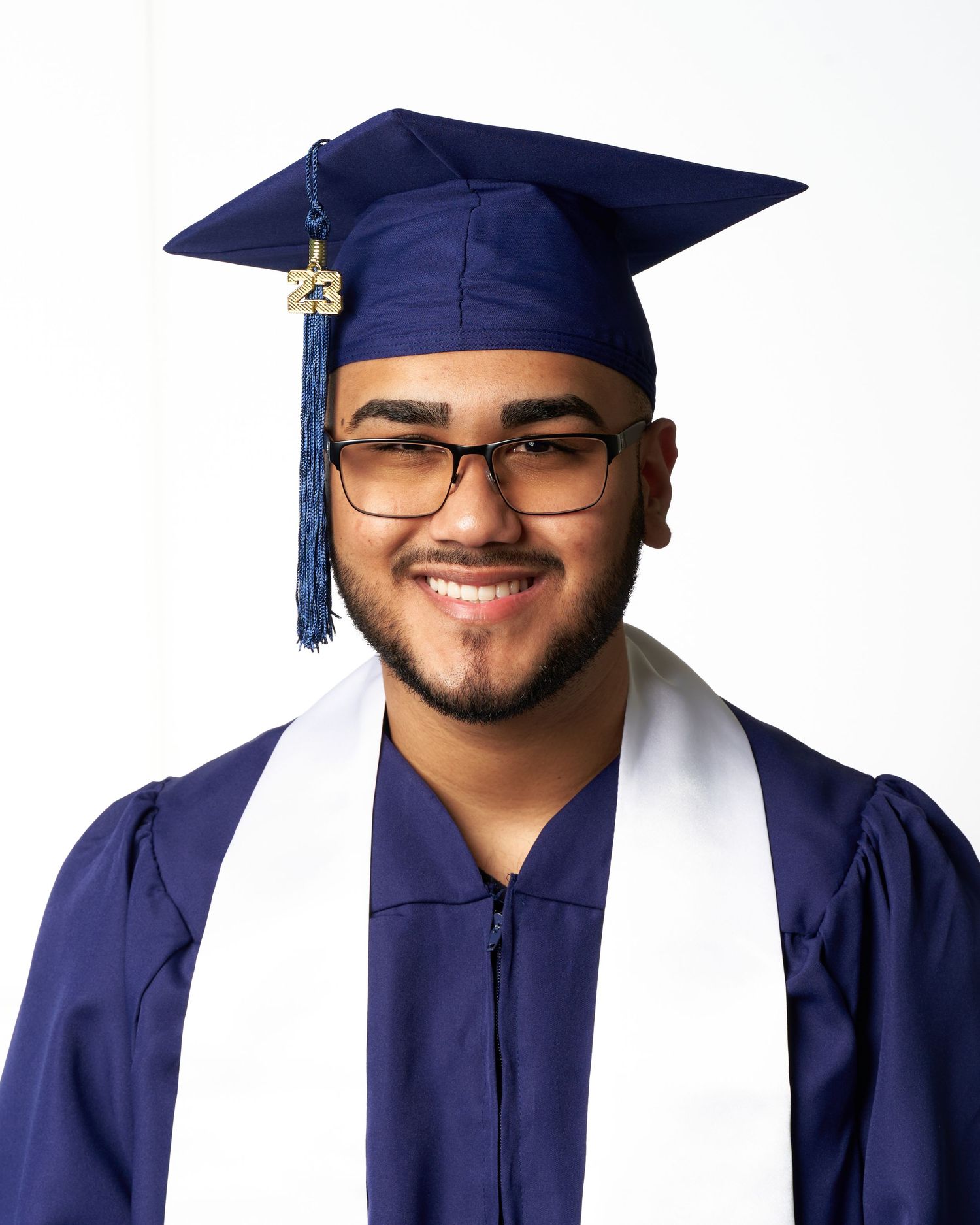 Graduate in navy blue cap and gown with tassel and glasses smiling during commencement ceremony.