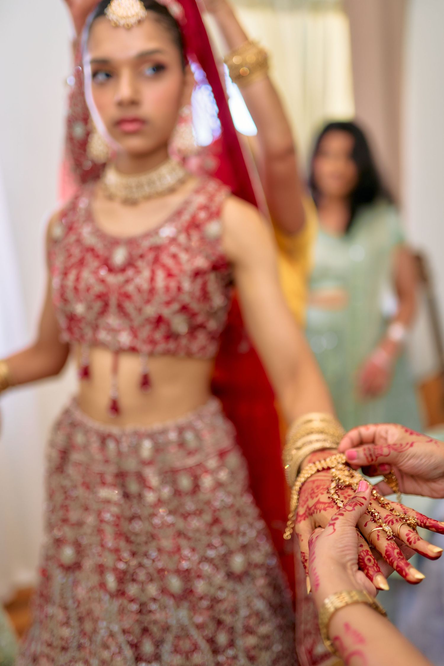 Close-up details of bride's traditional red lehenga and jewelry during Indian wedding preparations.