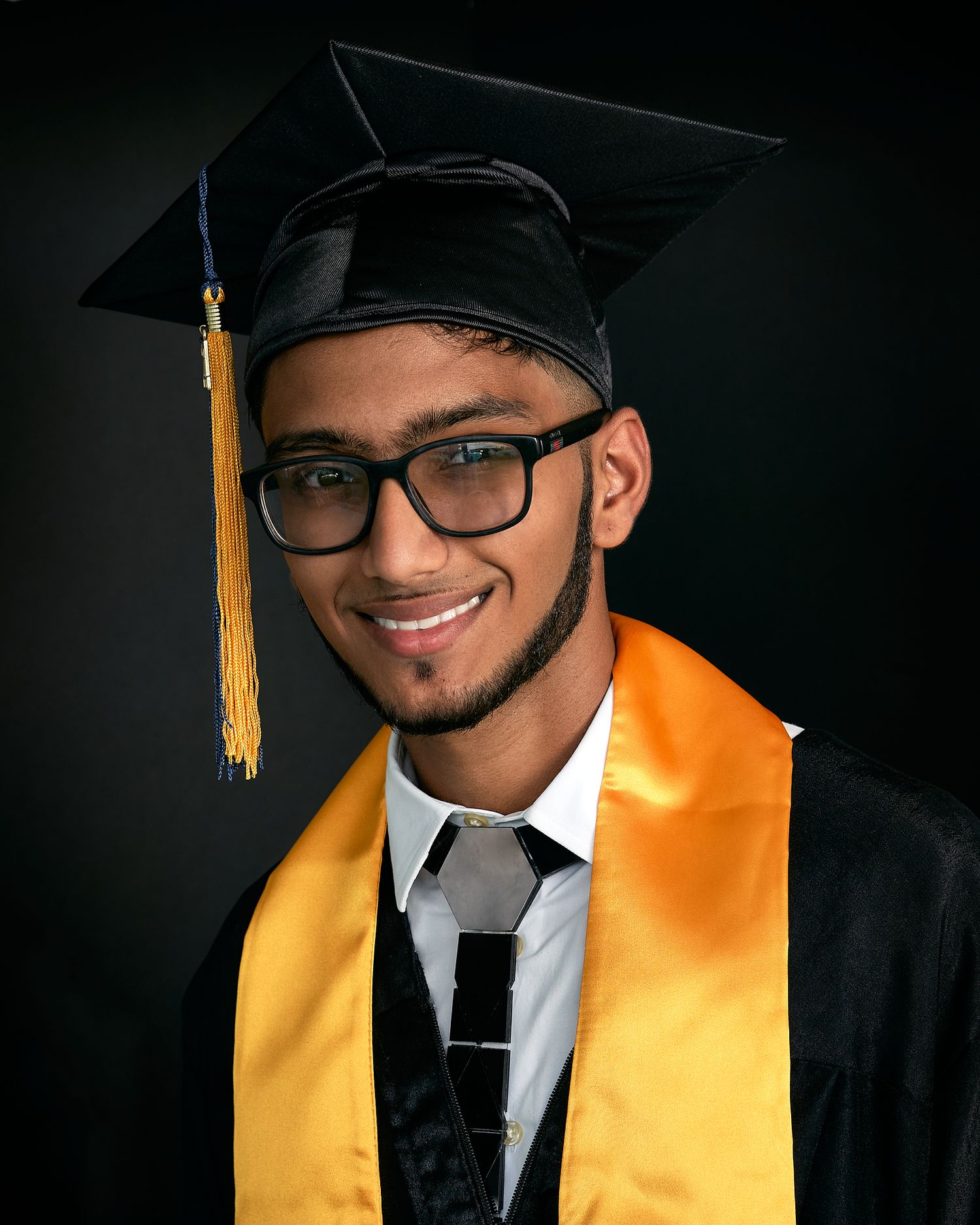 Graduate wearing cap and glasses with gold stole poses for professional photos.