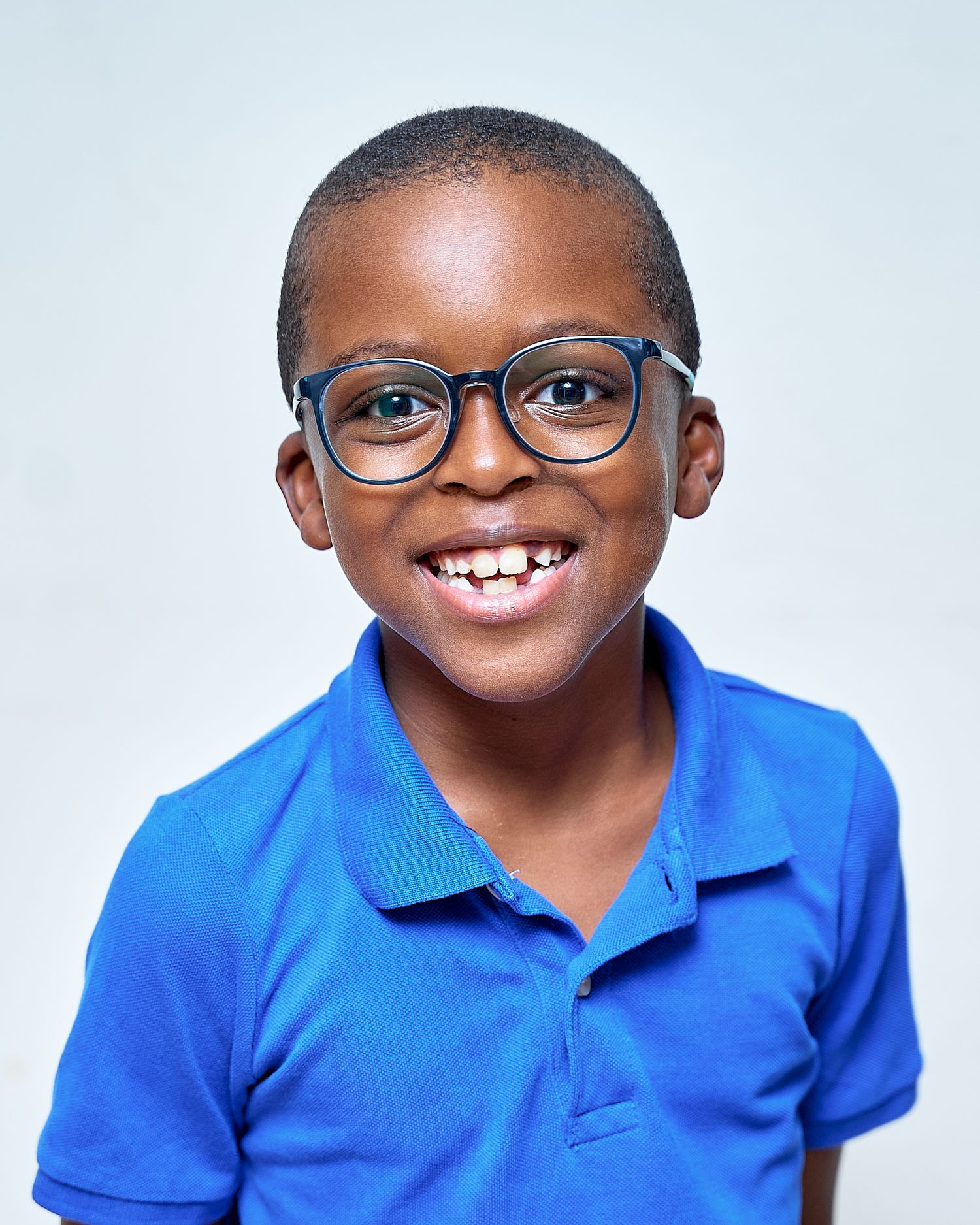 Child in blue polo shirt and glasses smiling brightly against white background.