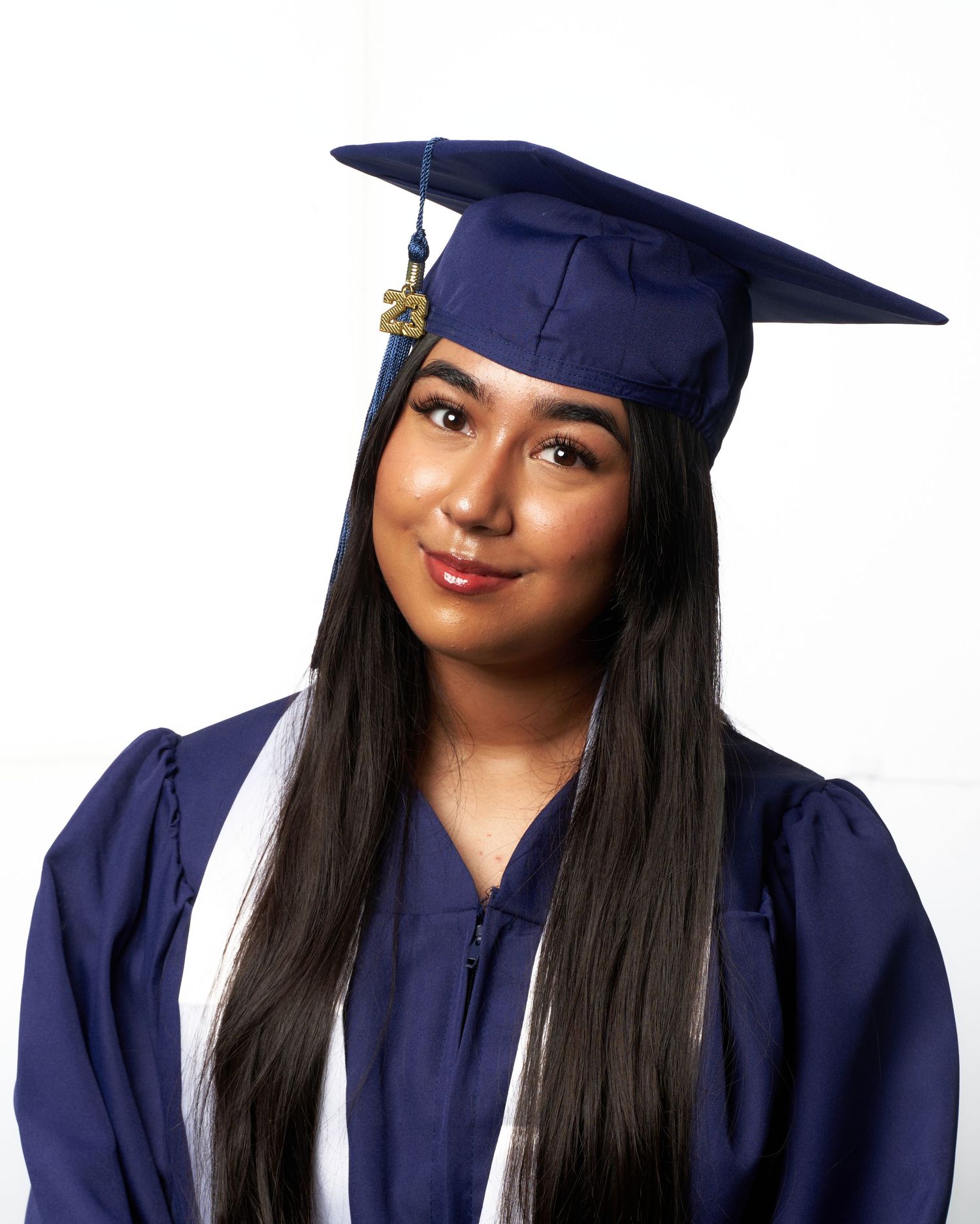 Graduate in navy blue cap and gown poses for professional graduation portraits against white backdrop.