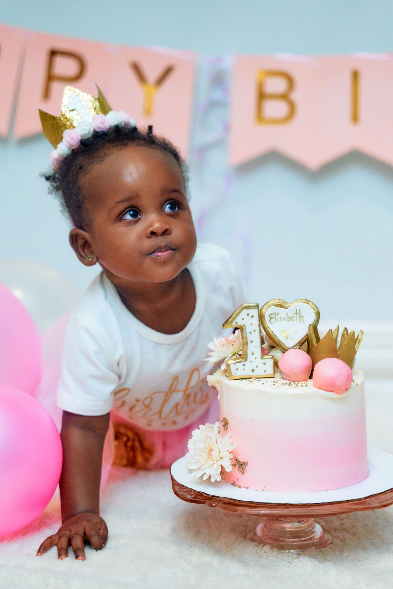 Pink and gold first birthday celebration with cake smash setup and decorative bunting banner.