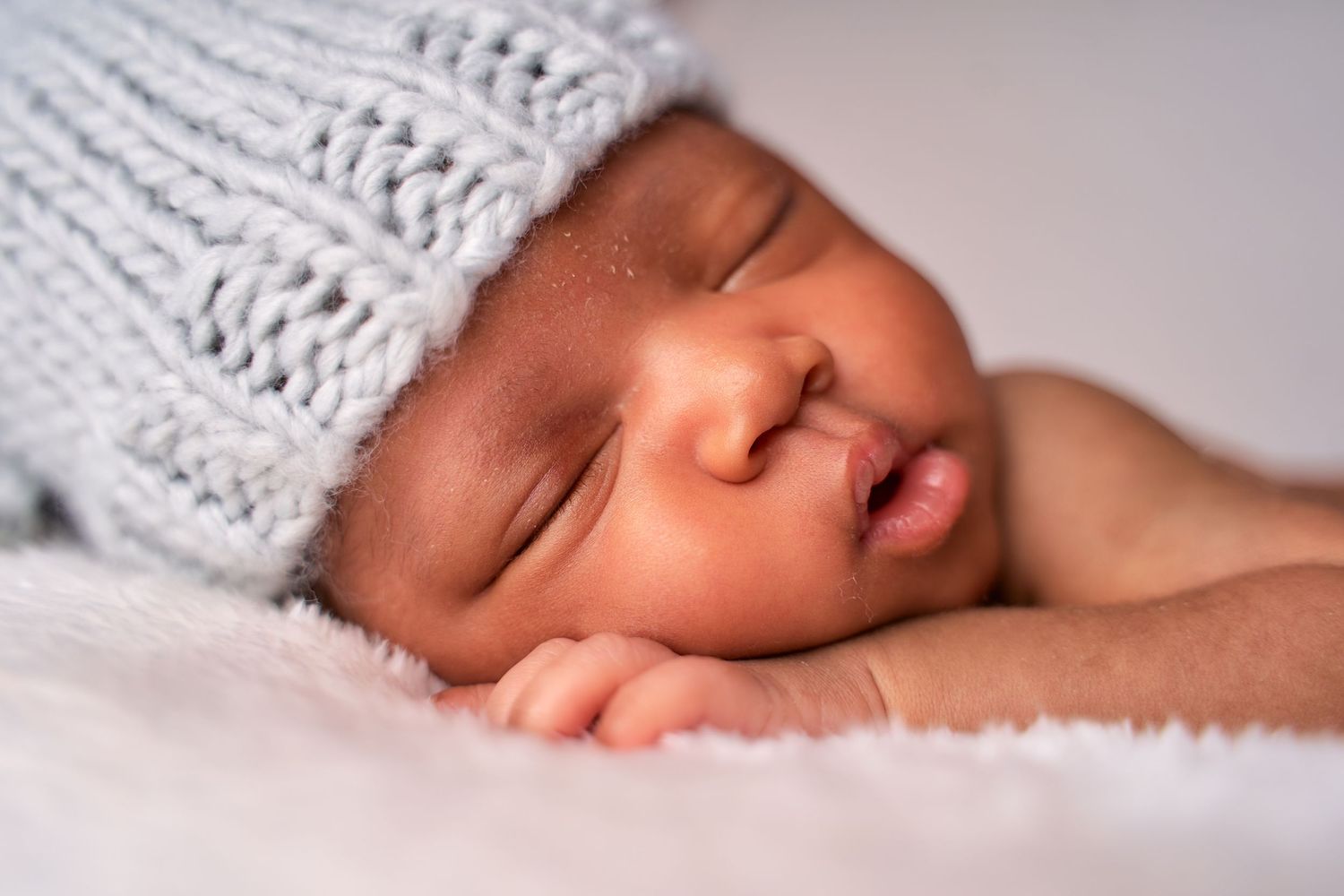 Peaceful sleeping newborn wearing soft knitted white hat rests on cozy blanket.