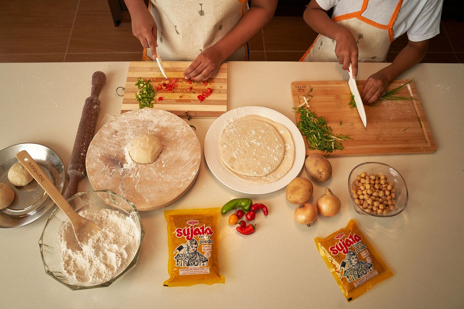 Overhead view of food preparation with cutting boards, flour, spices, vegetables and chickpeas on a kitchen counter.