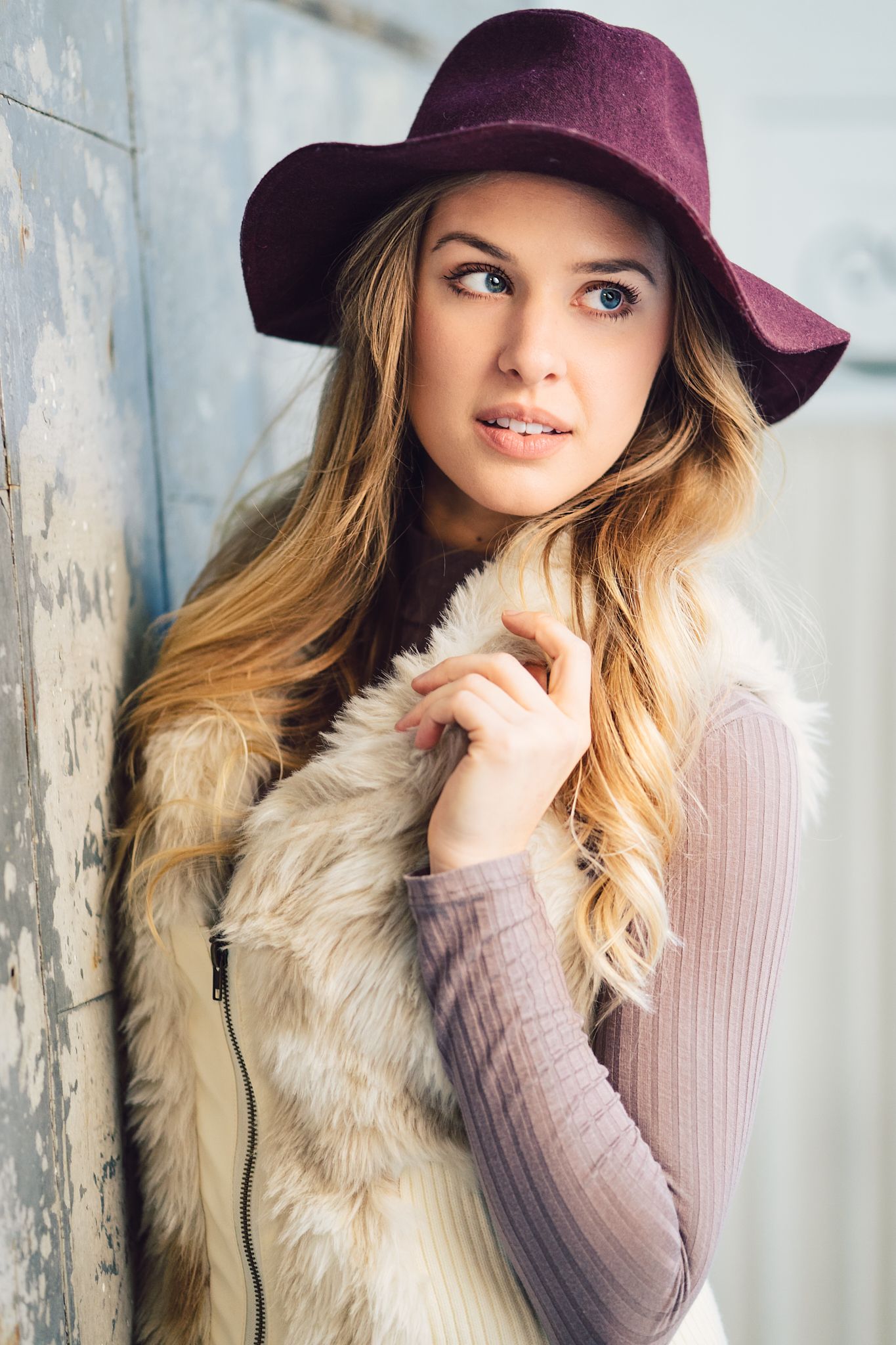 Stylish winter fashion portrait featuring burgundy hat and fur vest with soft natural lighting.