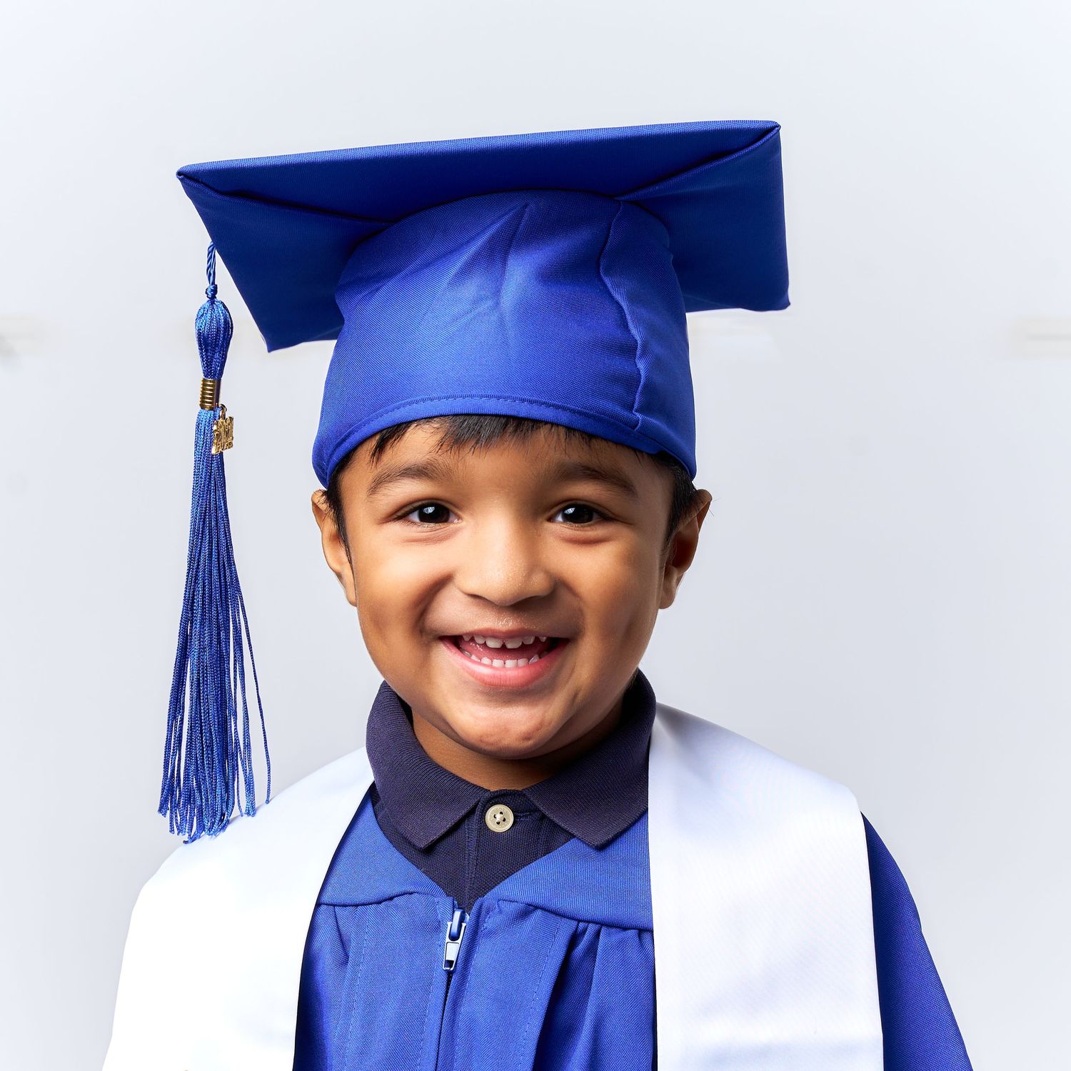 A young graduate in a royal blue cap and gown smiles brightly against a white background.