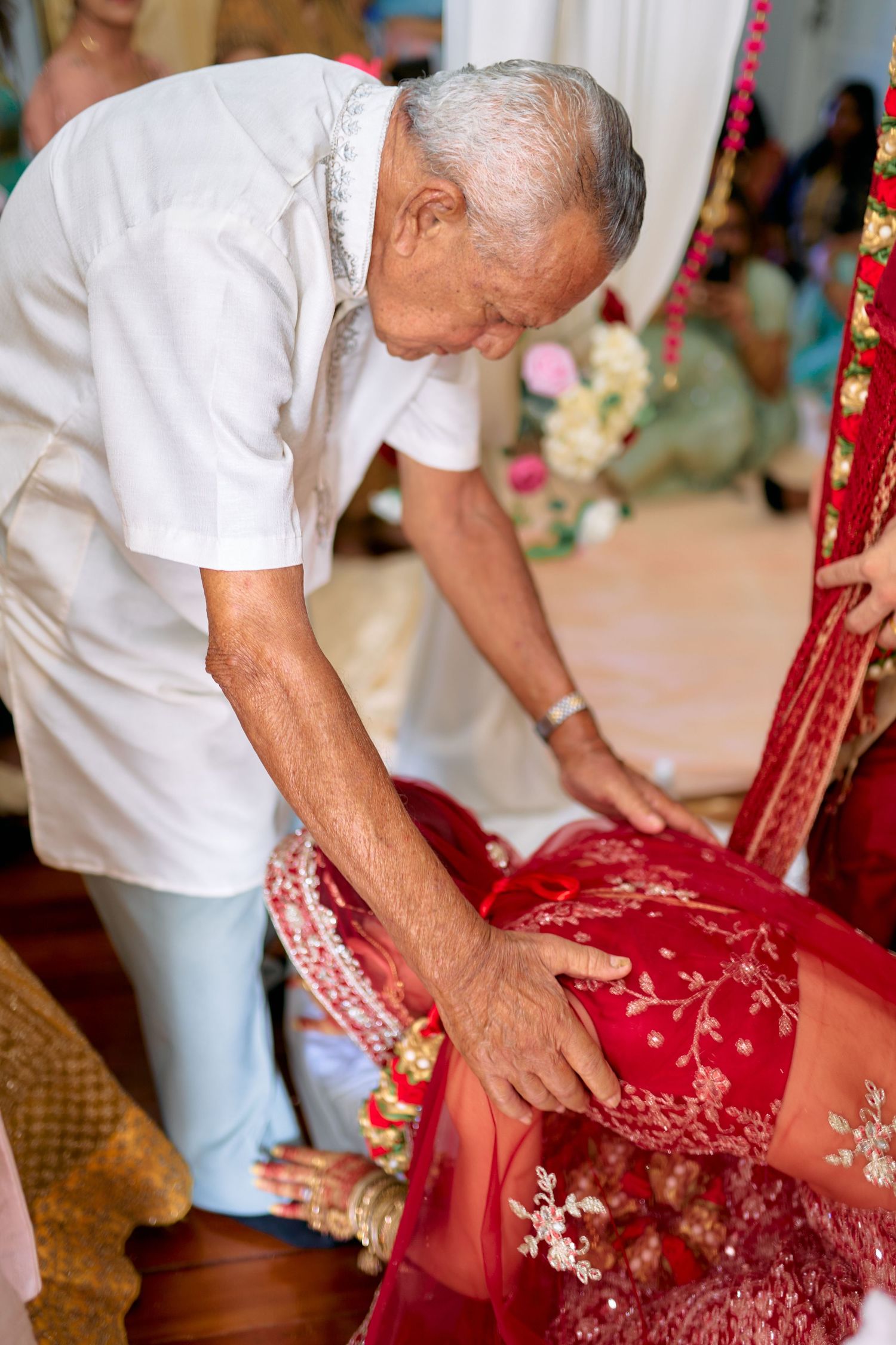 Elder adjusting traditional red bridal attire during wedding preparation.